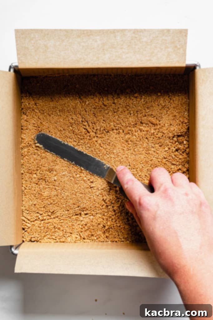 Graham cracker crumbs being pressed into a pan.
