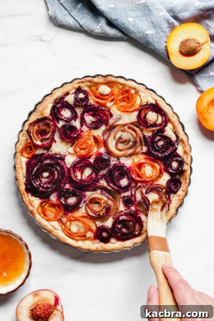 Brushing peach jam on top of the baked tart to provide a glaze and sheen, adding a professional finish.