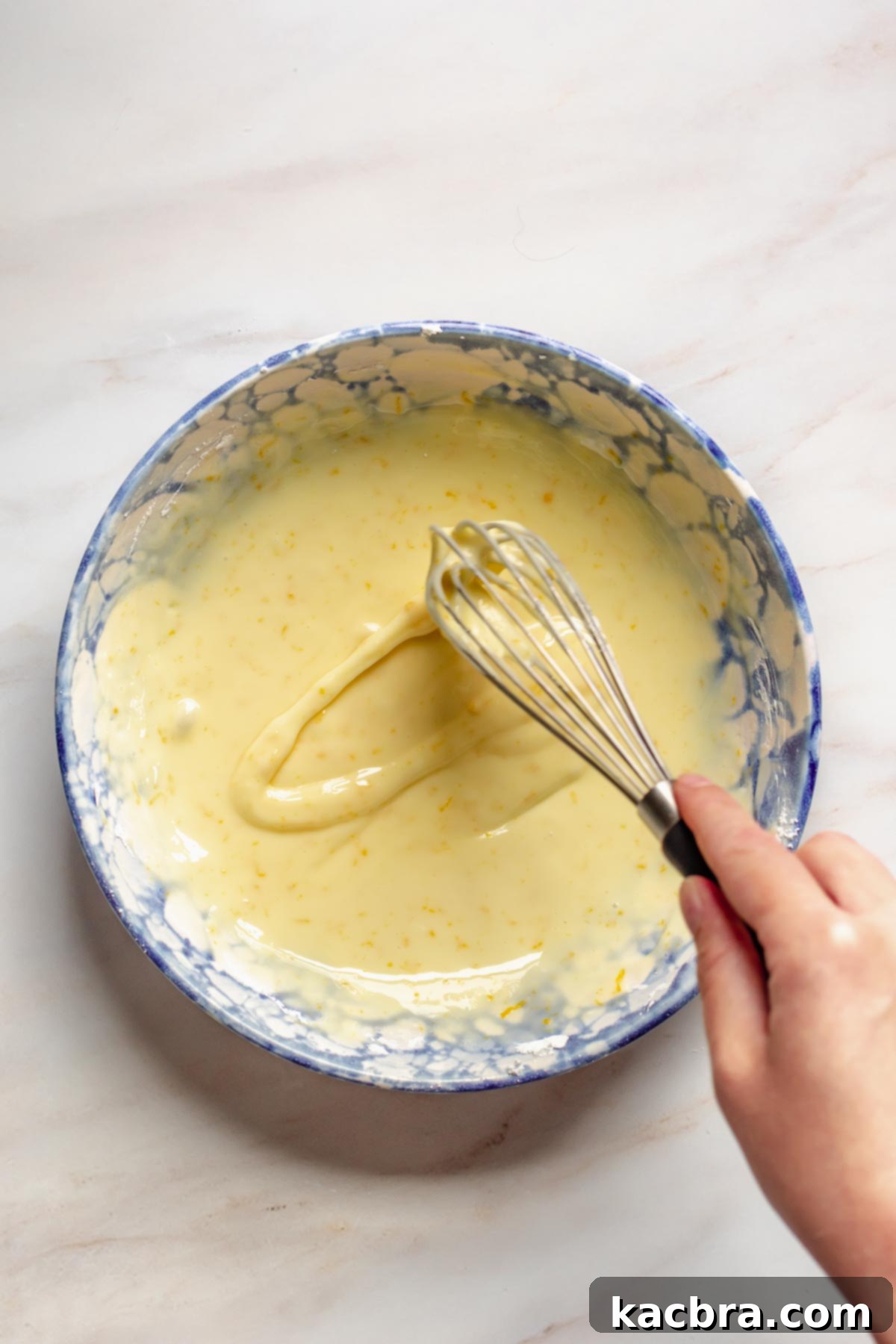 A whisk in a bowl of orange glaze.