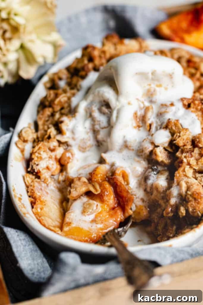A close-up of a golden-brown Brown Butter Peach Crisp, fresh from the oven, with a scoop of melting vanilla ice cream on top.