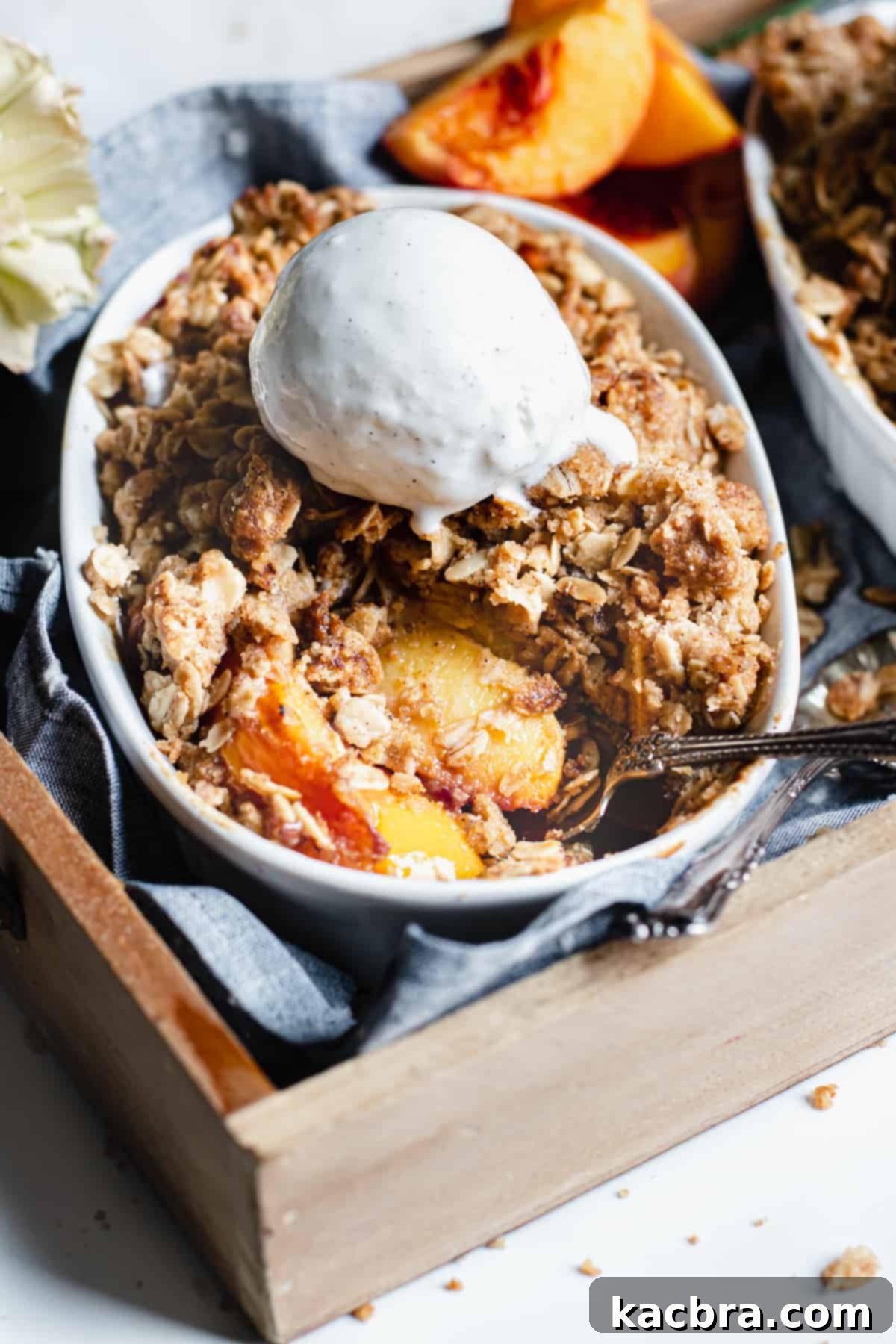 A close-up of a rustic pan of brown butter peach crisp, with a serving spoon poised to scoop out a portion, highlighting the golden crumble and juicy peaches.