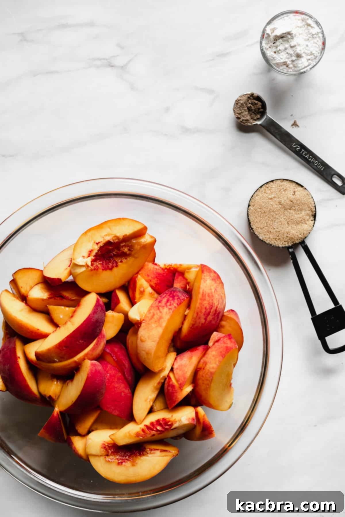 Bowl of freshly sliced peaches with brown sugar, cardamom and flour next to it, ready to be tossed.