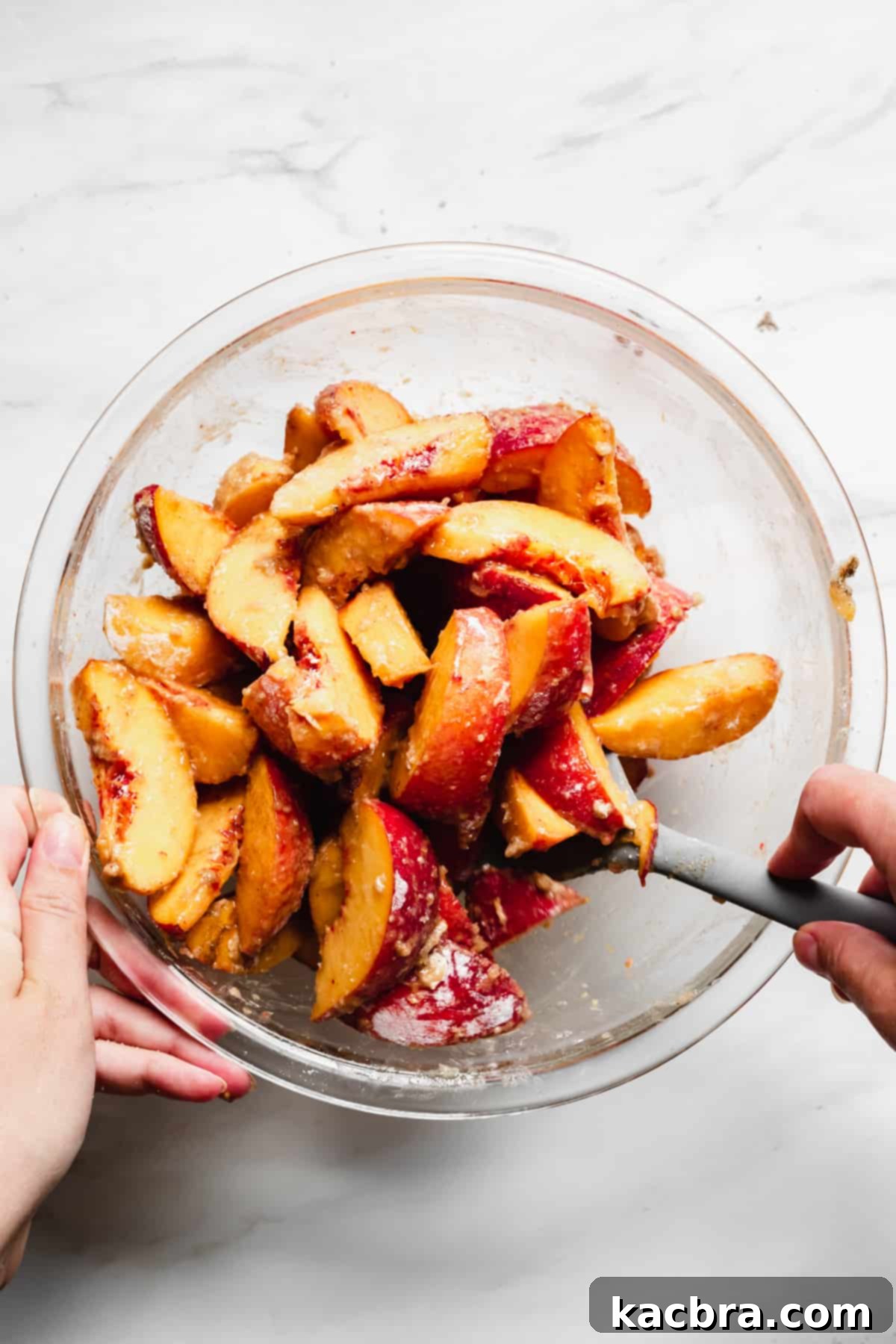 Sliced peaches fully coated with brown sugar, spices, and flour in a mixing bowl.