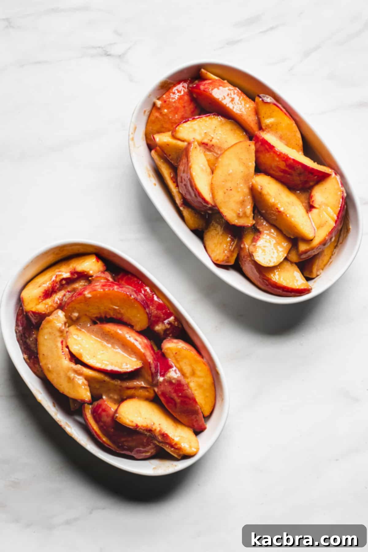 Prepared peaches sitting in two small oval casserole dishes, ready for the topping.