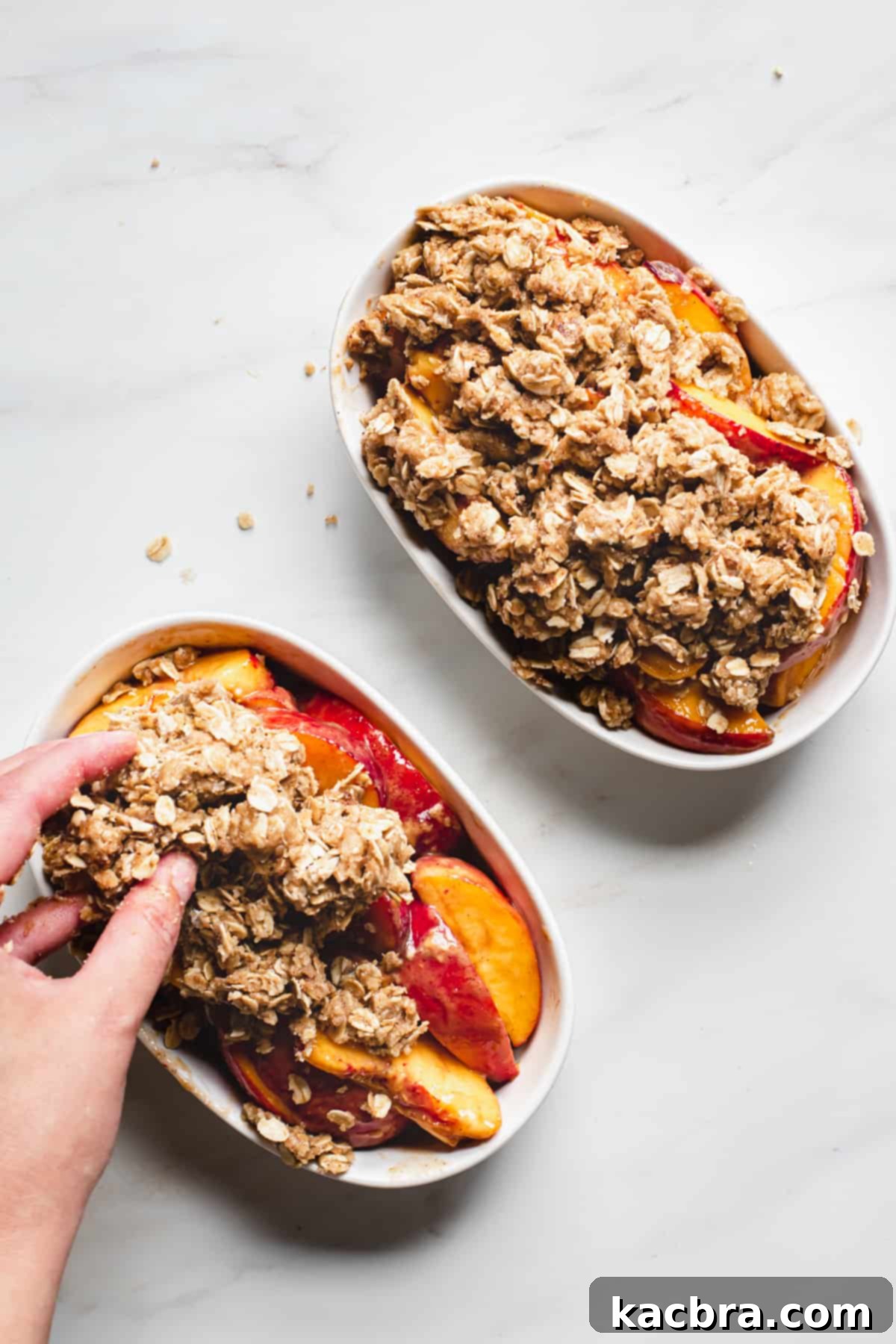The crumble topping being sprinkled evenly over the peaches in the baking dishes.