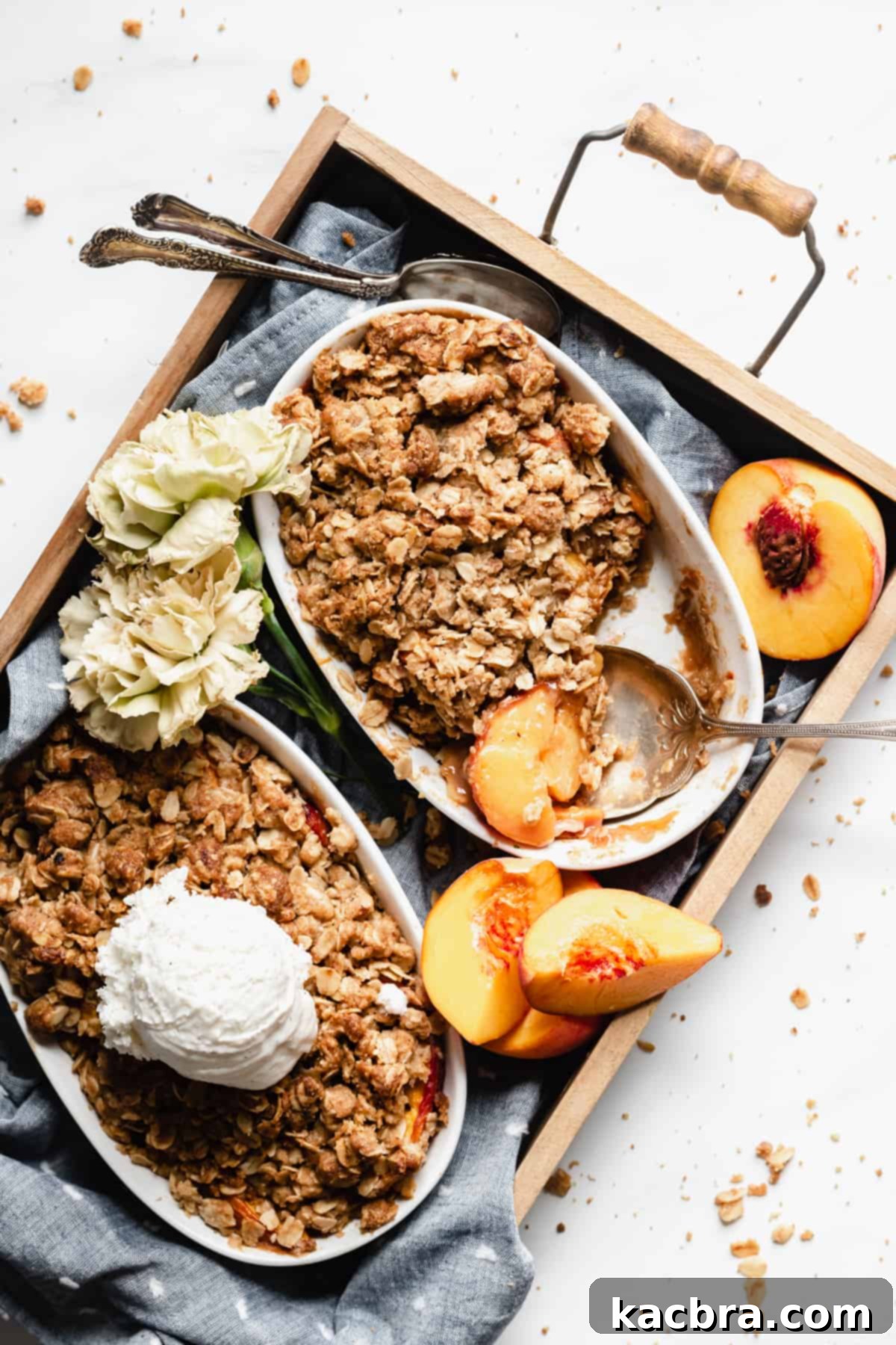 An overhead shot of two pans of peach crisp in a rustic basket, with a large scoop already removed from one, revealing the juicy peaches beneath the golden crumble.