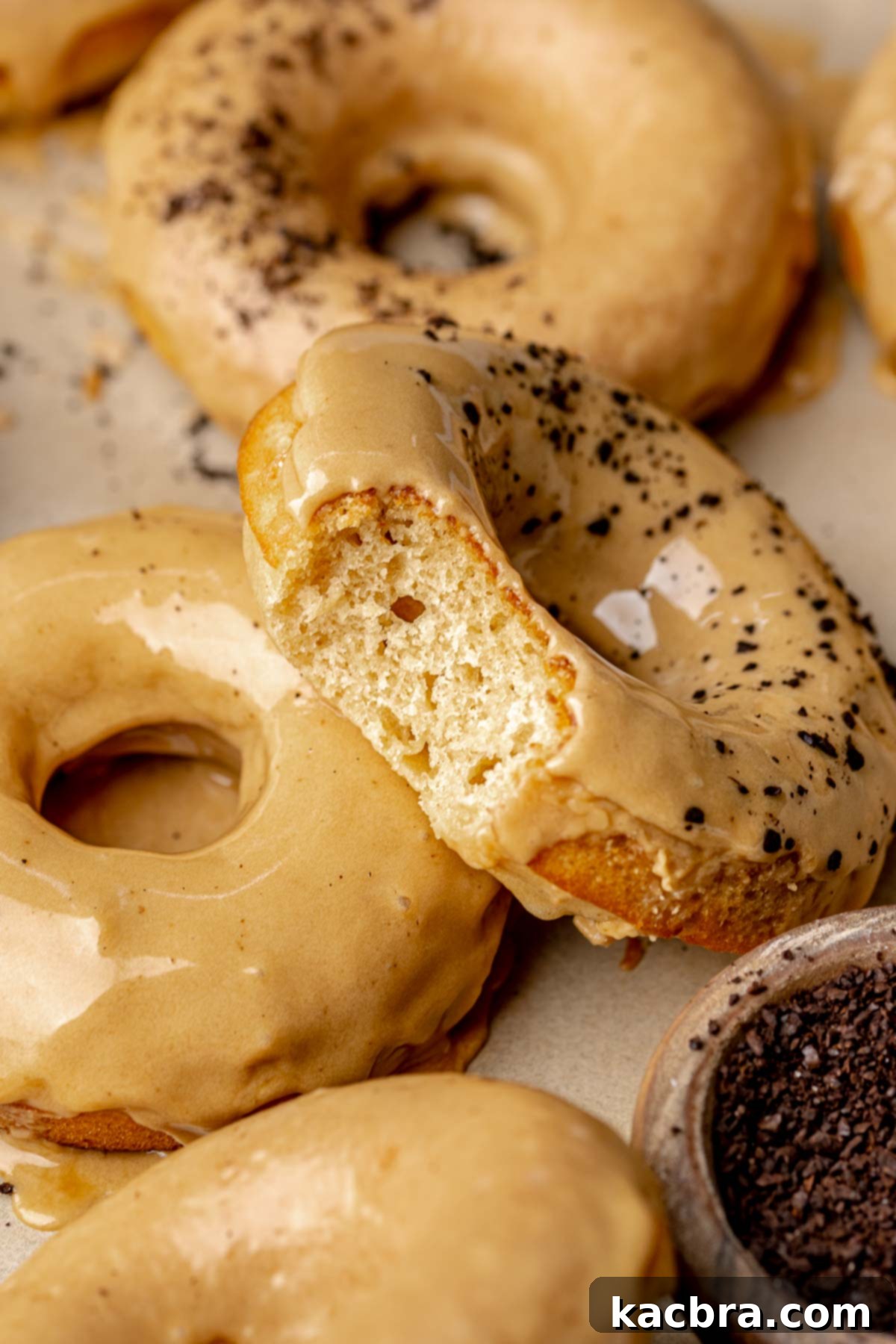 A bite removed from a coffee donut leaning on another glazed donut.
