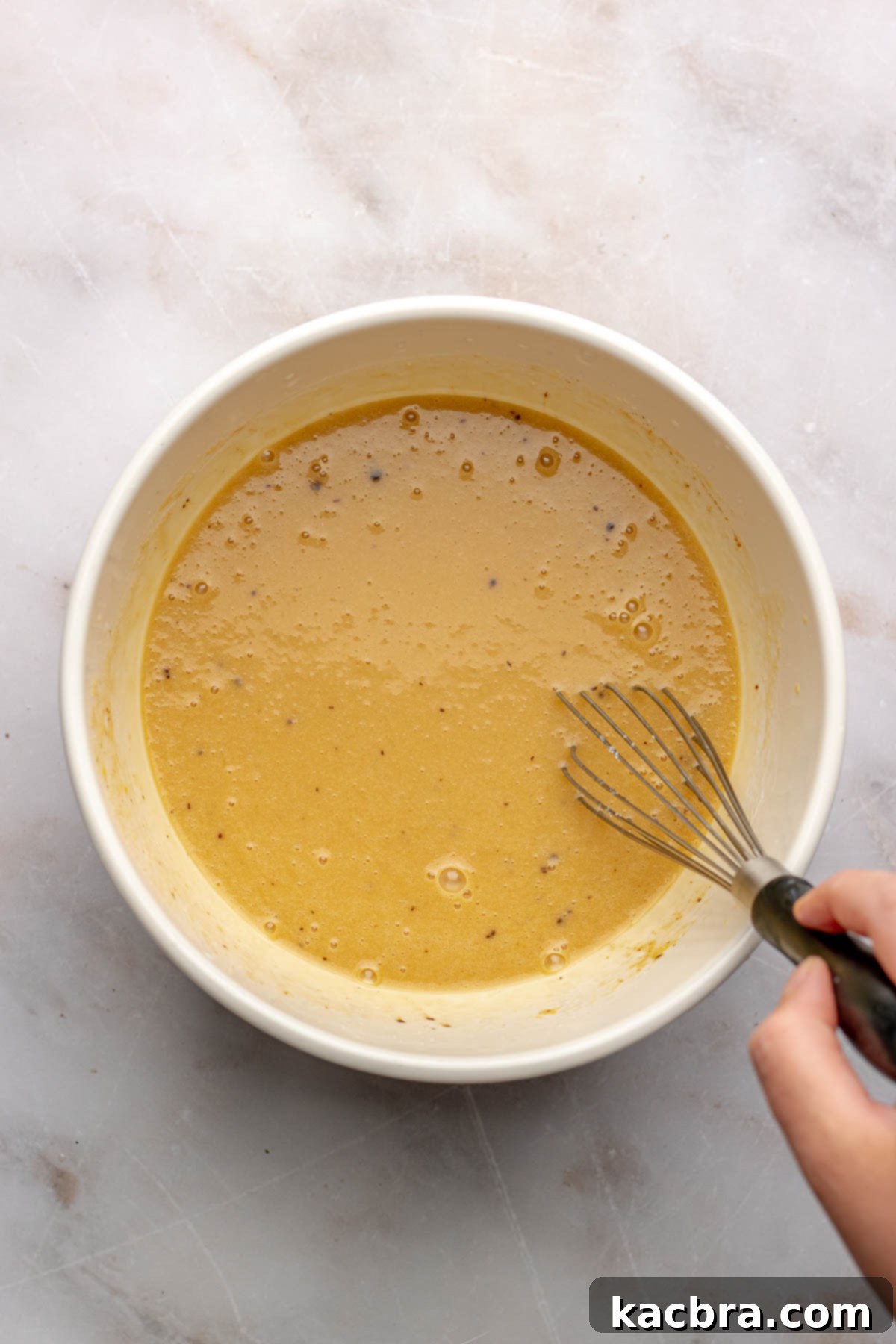 A whisk mixes wet ingredients in a bowl, showing the beginning of the donut batter preparation.