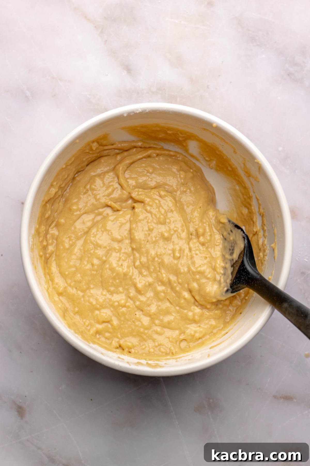 A spatula folds together donut batter in a bowl, demonstrating the gentle mixing technique.