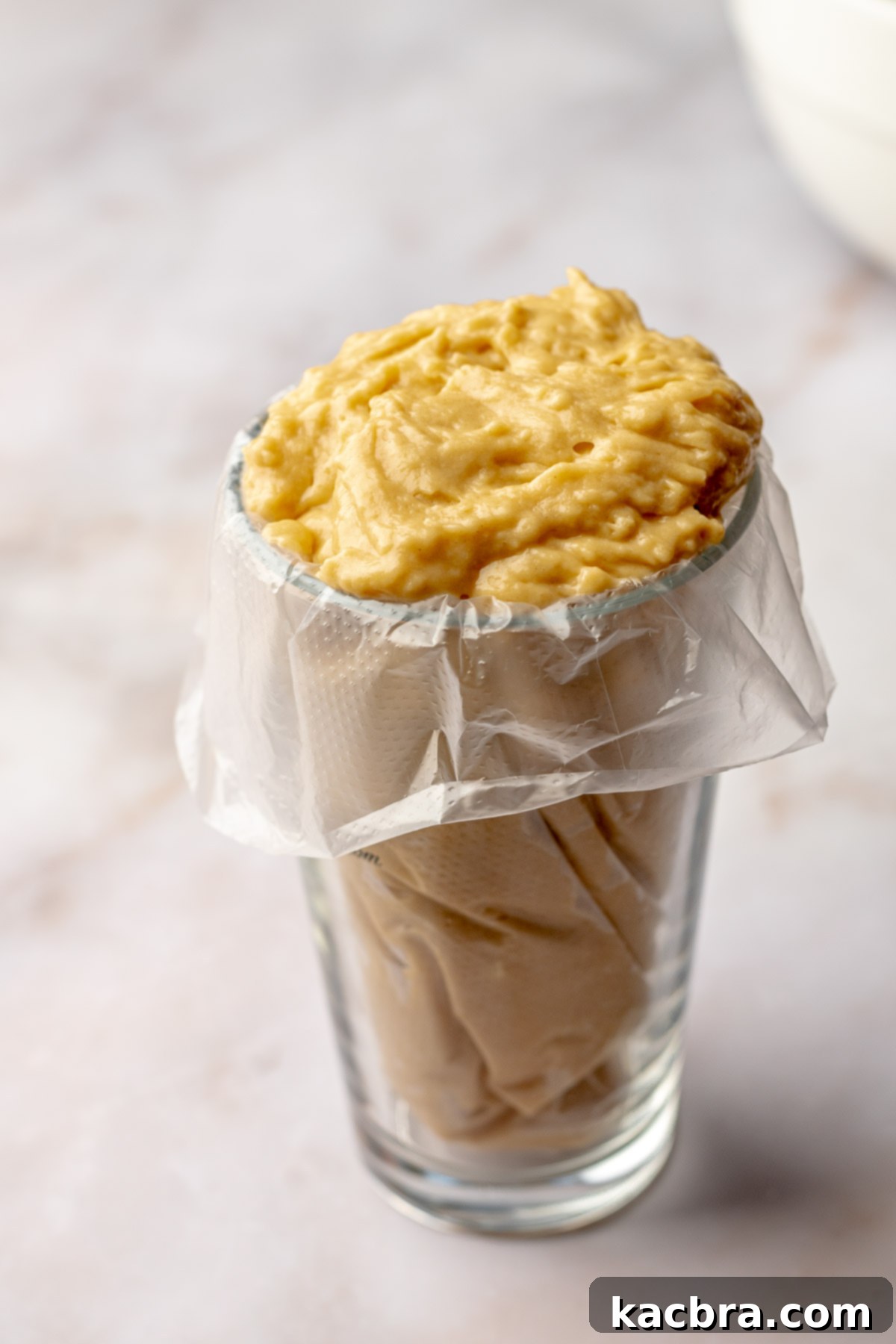 Donut batter in a piping bag placed in a cup, ready for filling the pan.