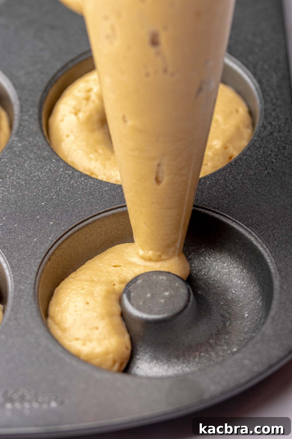 Donut batter being piped into a greased donut pan, showing the technique for even distribution.