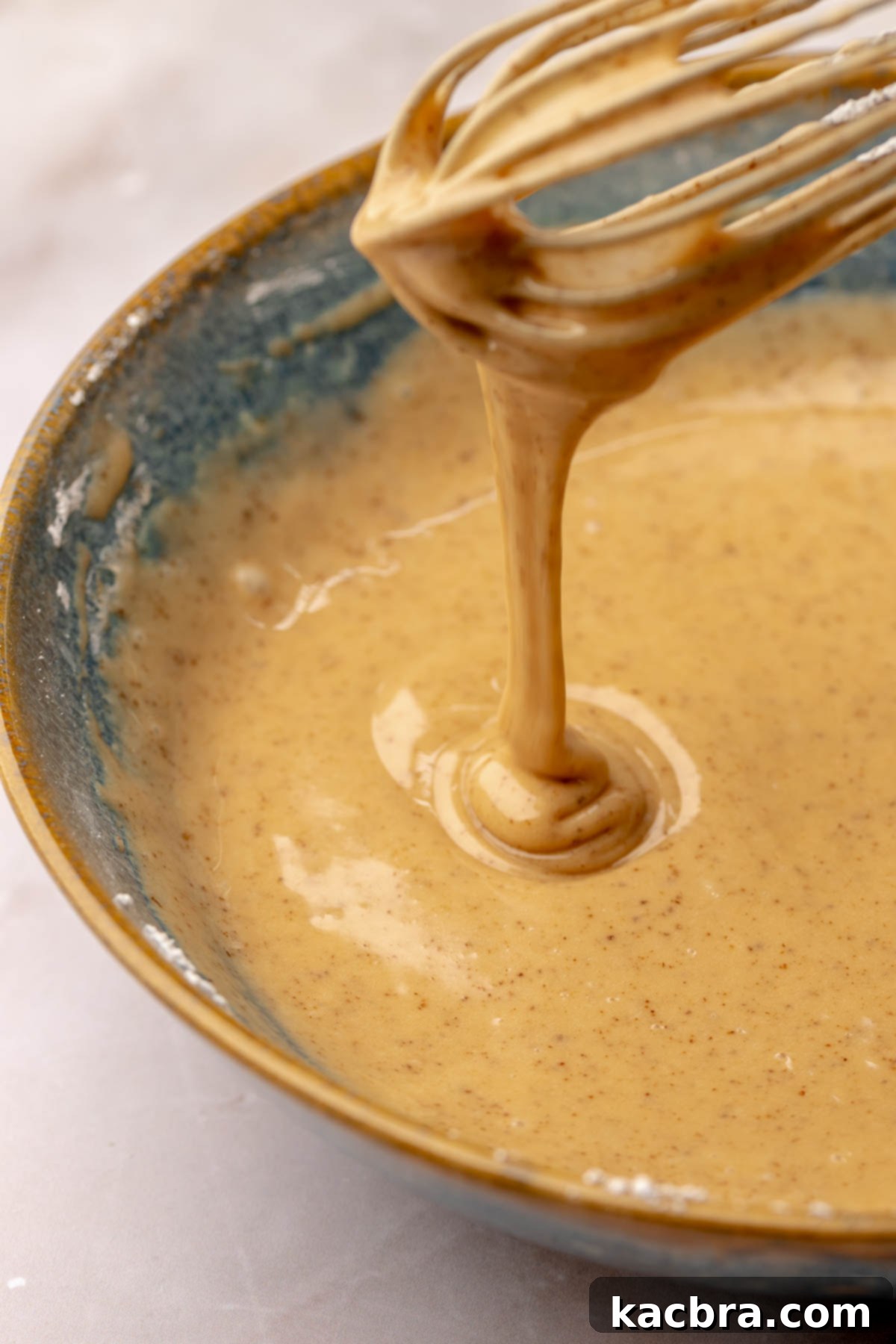 Coffee glaze dripping off of a whisk, showing the ideal thick consistency.