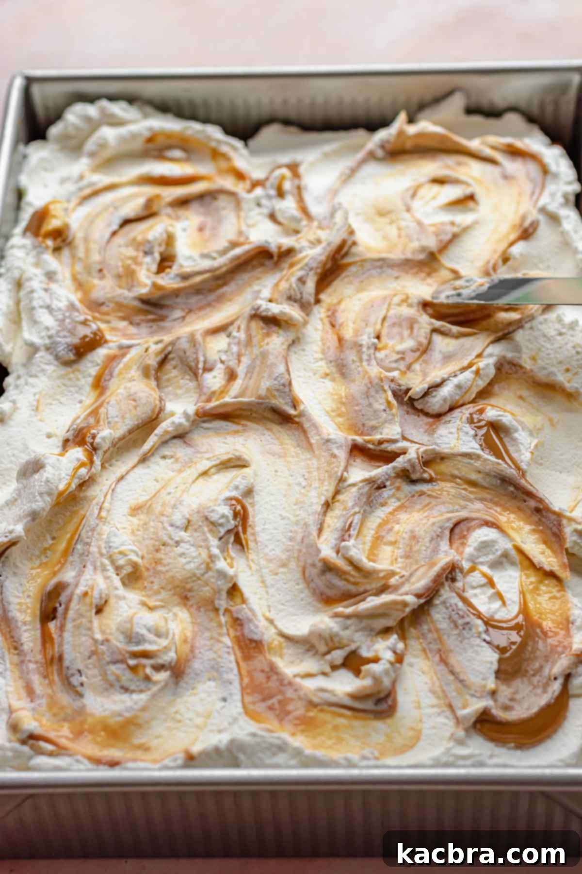 An offset spatula artfully swirls the dulce de leche into the whipped cream on top of the cake, creating an elegant marbled effect.