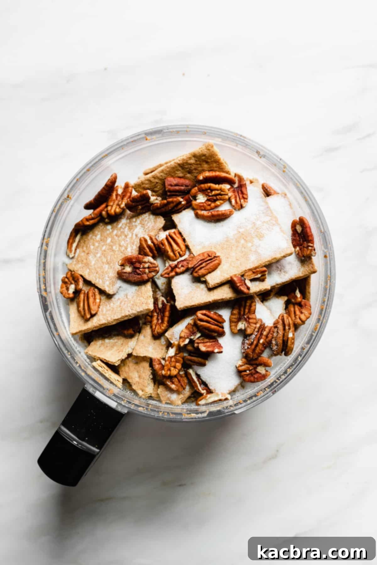 Decadent Caramel Pecan Cheesecake 5 Graham crackers, pecans, and sugar being processed together in a food processor to create a fine crumb mixture for the cheesecake crust.