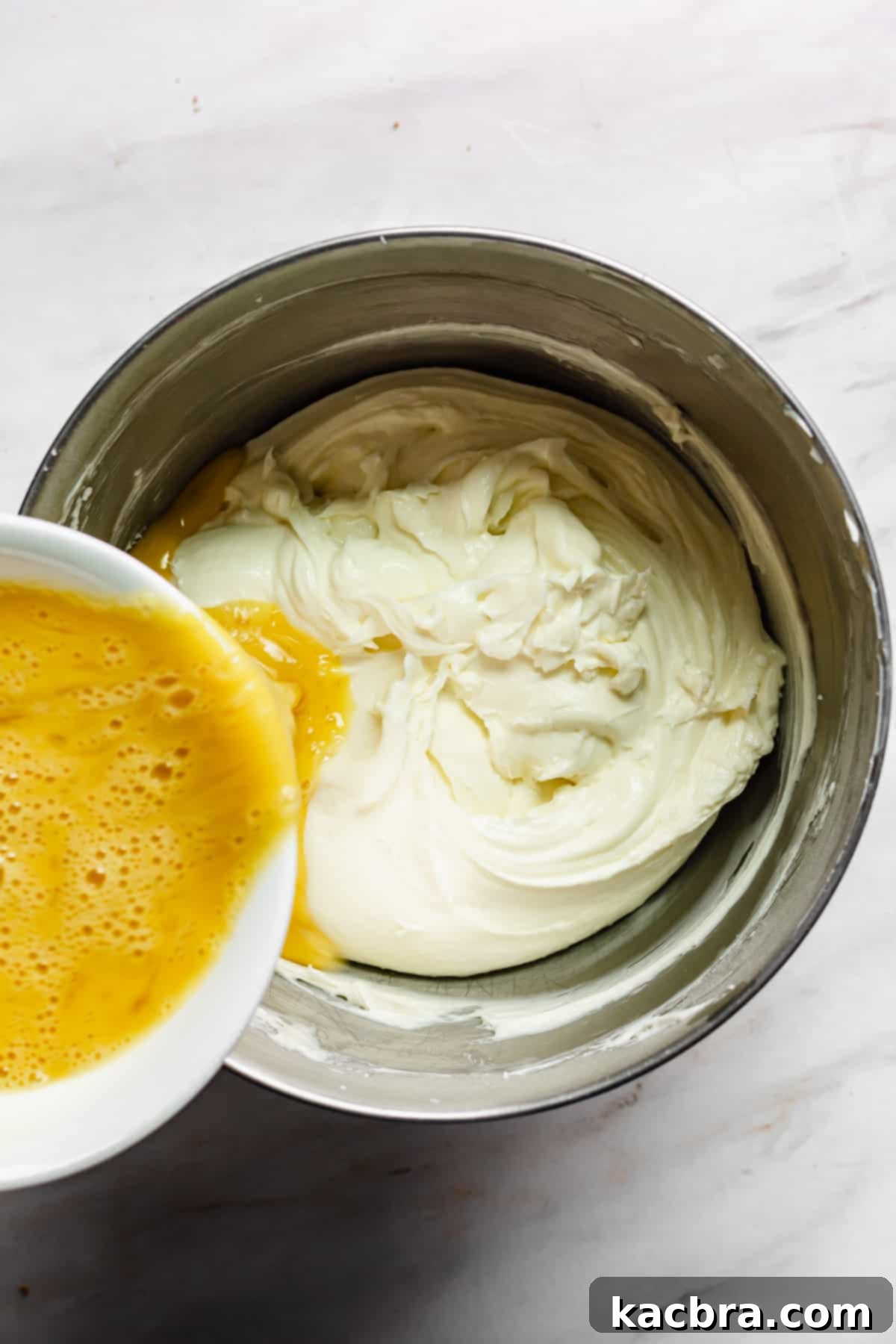 Decadent Caramel Pecan Cheesecake 8 Whisked eggs being slowly drizzled into the creamy cheesecake batter in a stand mixer on low speed.