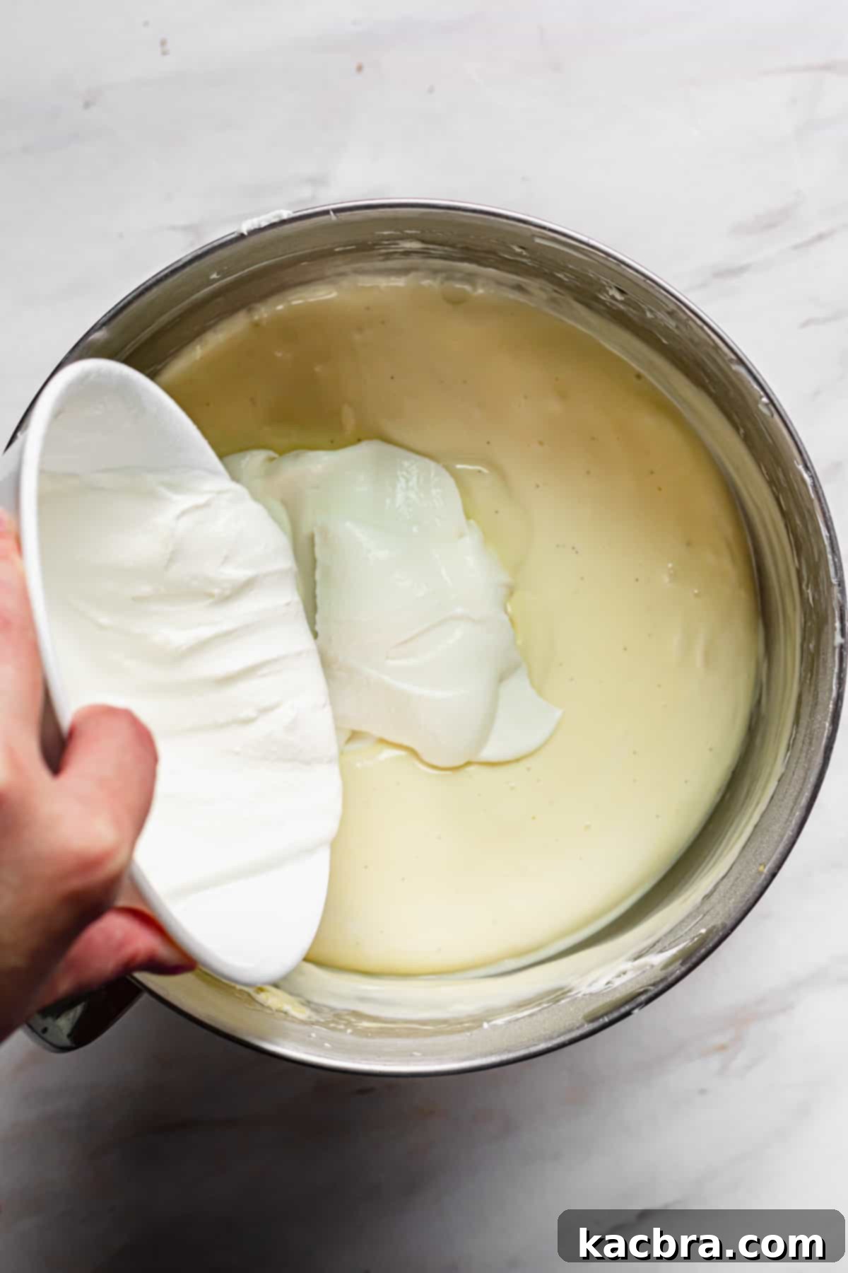 Decadent Caramel Pecan Cheesecake 9 Room temperature sour cream being gently folded into the cheesecake batter by hand with a spatula.