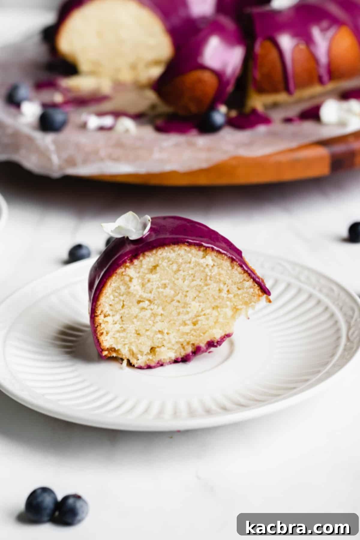 Velvet Lemon Ricotta with Bursting Blueberry Glaze 10 A close-up, straight-on shot of a slice of lemon pound cake with its vibrant blueberry glaze, elegantly placed on a plate.