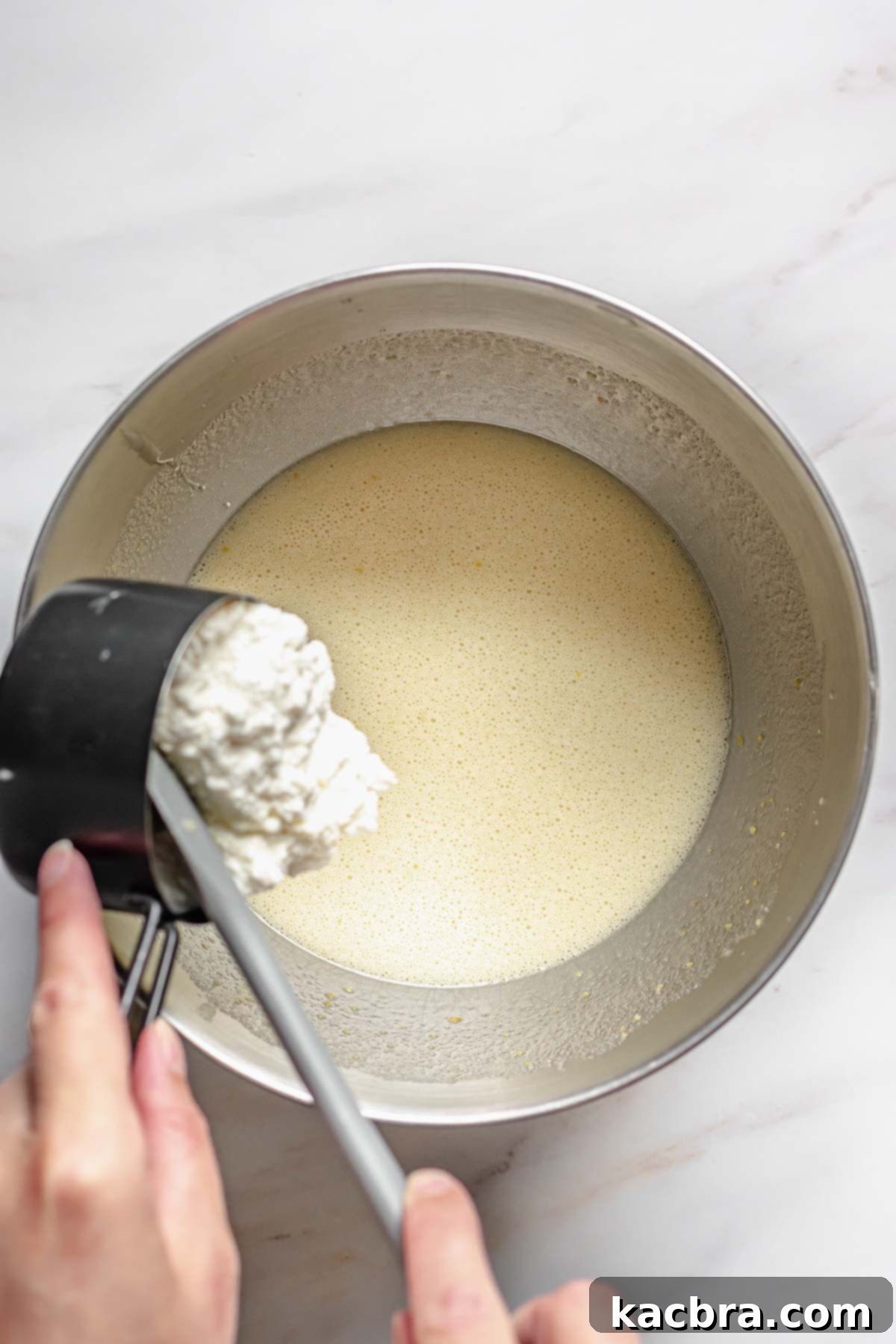 Velvet Lemon Ricotta with Bursting Blueberry Glaze 5 Ricotta cheese being carefully added to the vibrant cake batter, contributing to its moist and tender texture.