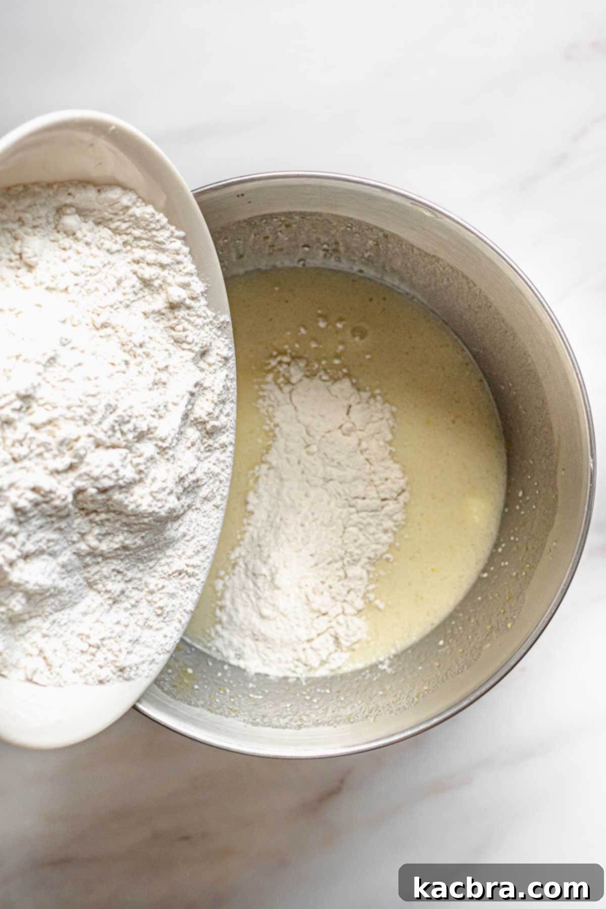 Velvet Lemon Ricotta with Bursting Blueberry Glaze 6 Dry ingredients being gently poured into the wet batter, showcasing the careful mixing process for the perfect cake.