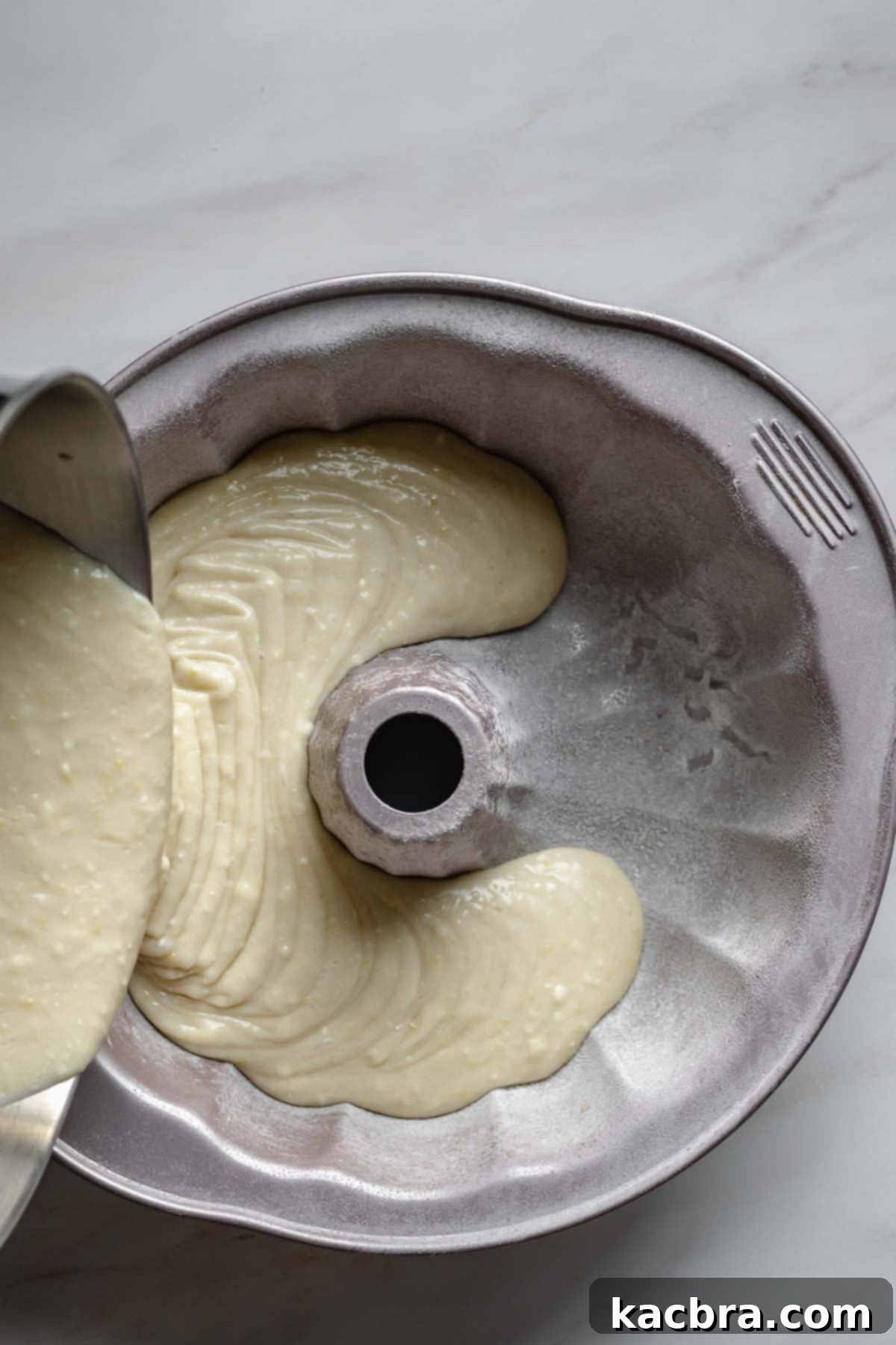 Velvet Lemon Ricotta with Bursting Blueberry Glaze 7 Lemon ricotta cake batter smoothly pouring into a meticulously prepared bundt pan, ready for baking.