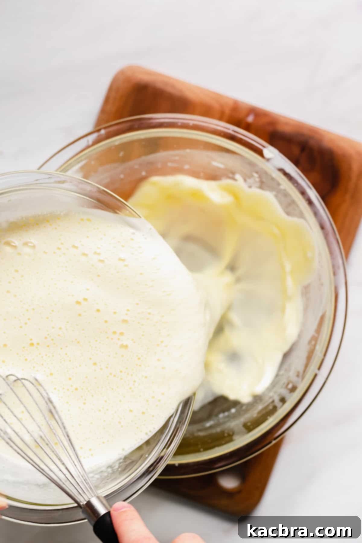 The tempered custard mixture being poured into the top bowl of a double boiler for gentle cooking.