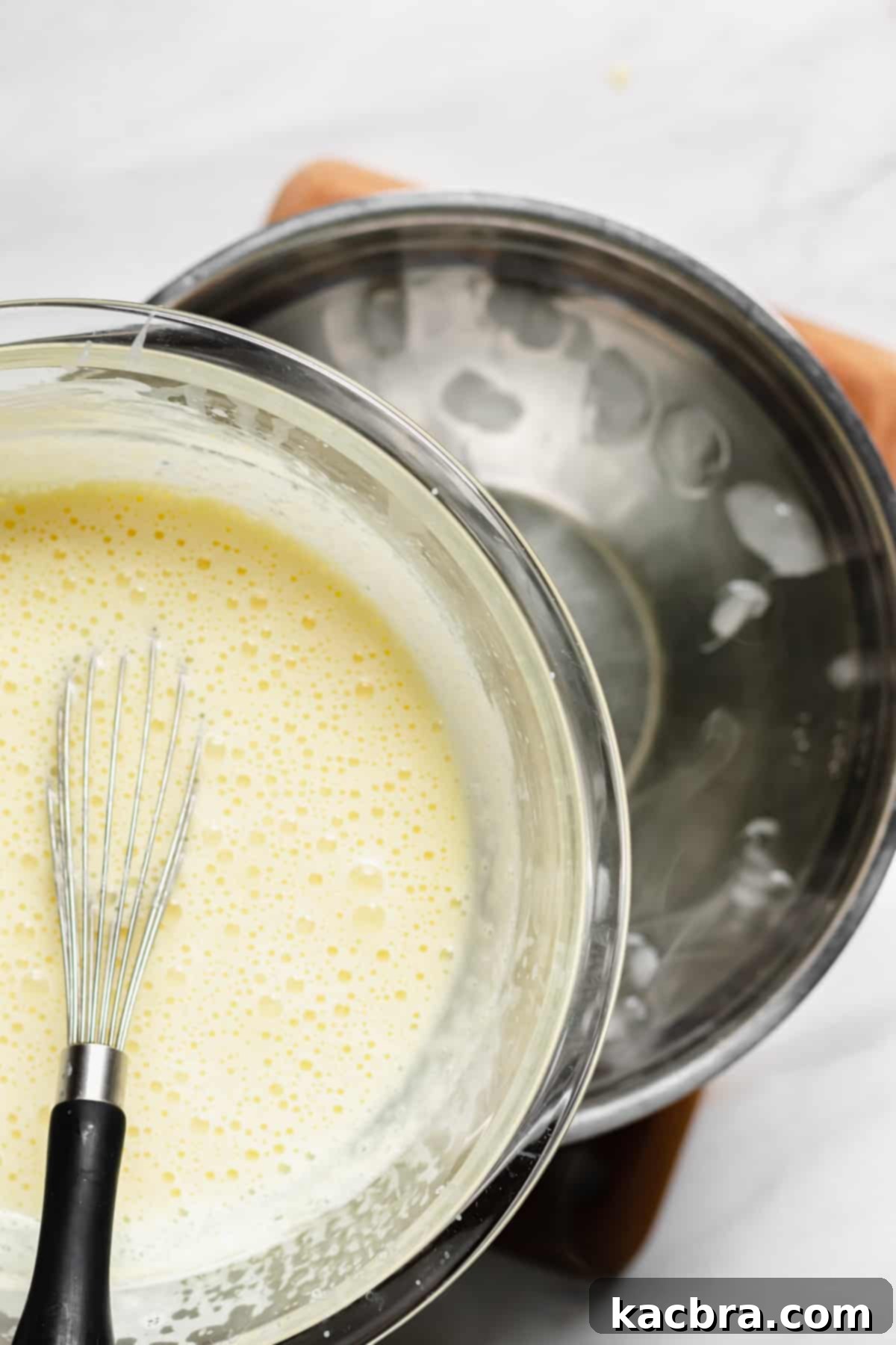 Bowl of hot vanilla sauce being carefully placed onto an ice water bath to halt the cooking process.