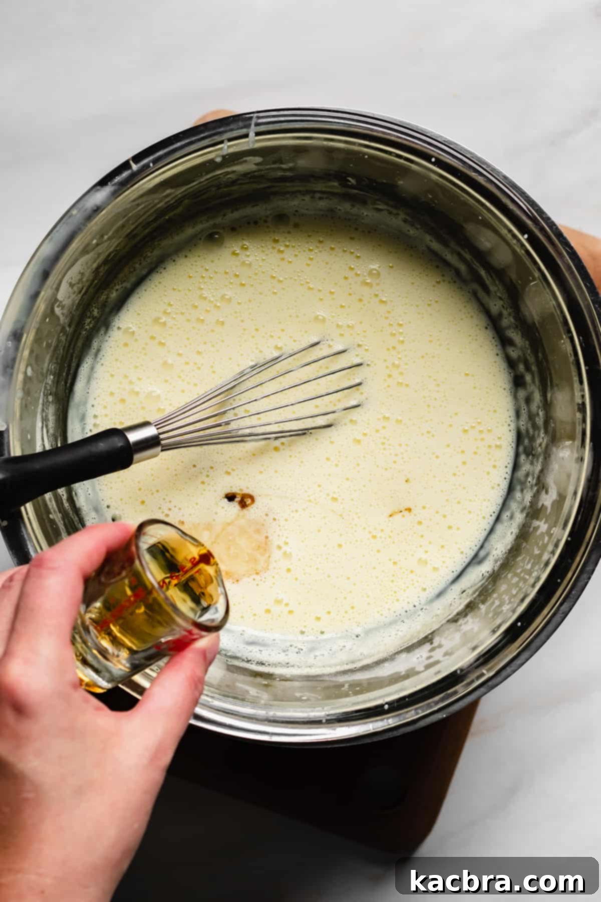 Bourbon being gently poured into the cooled vanilla custard sauce and mixed.