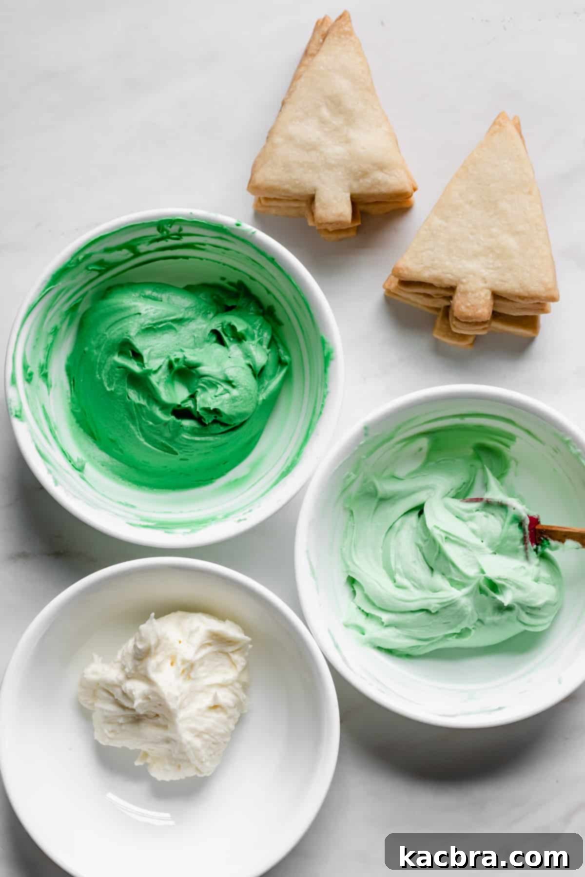 Dark green, light green, and white frosting in bowls.