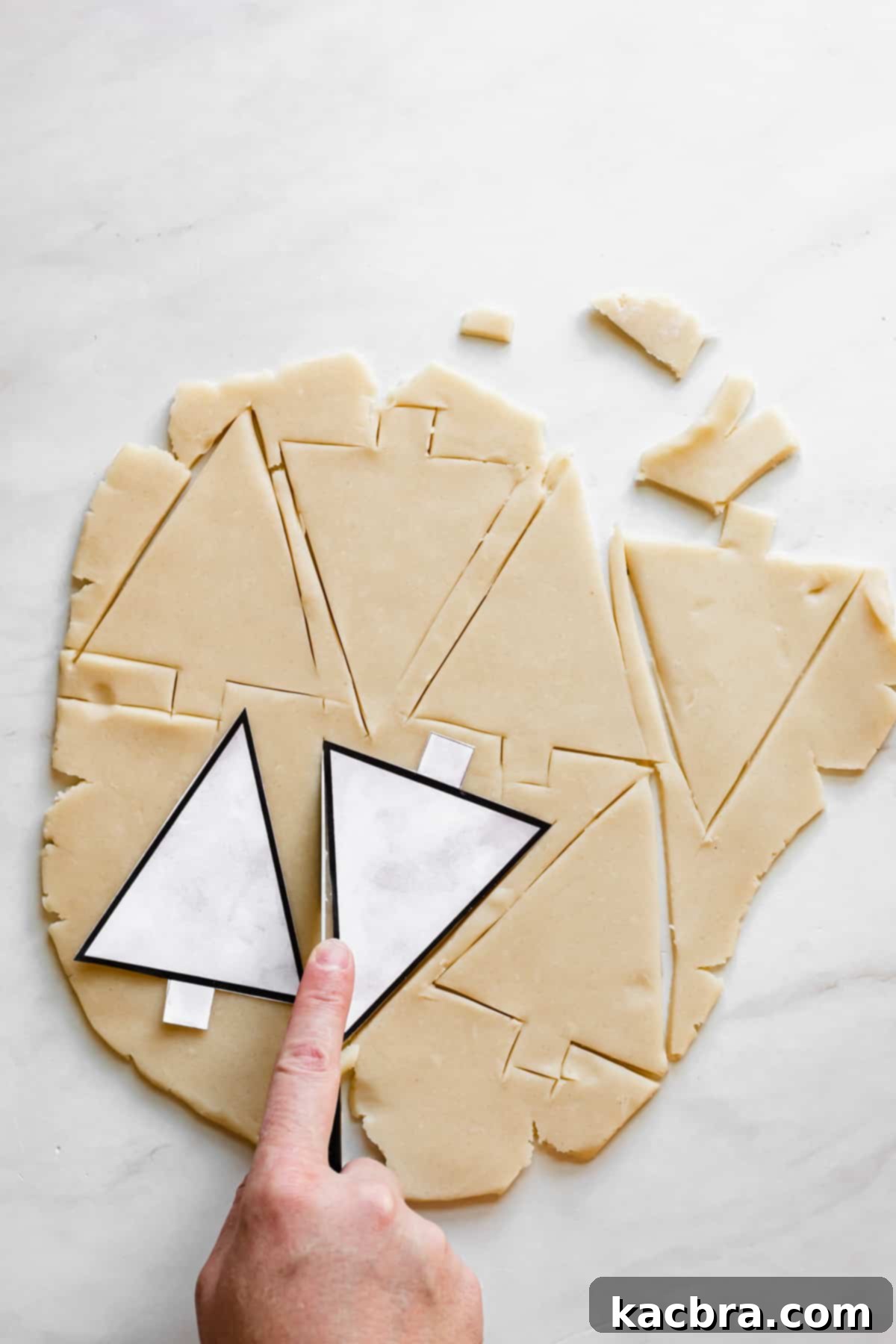 A hand cuts out Christmas tree cookies from the template