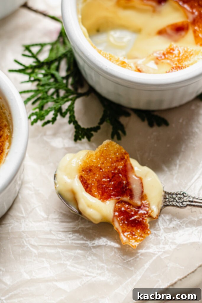 Two ramekins of Eggnog Crème Brûlée, one with a spoon breaking the caramelized top.