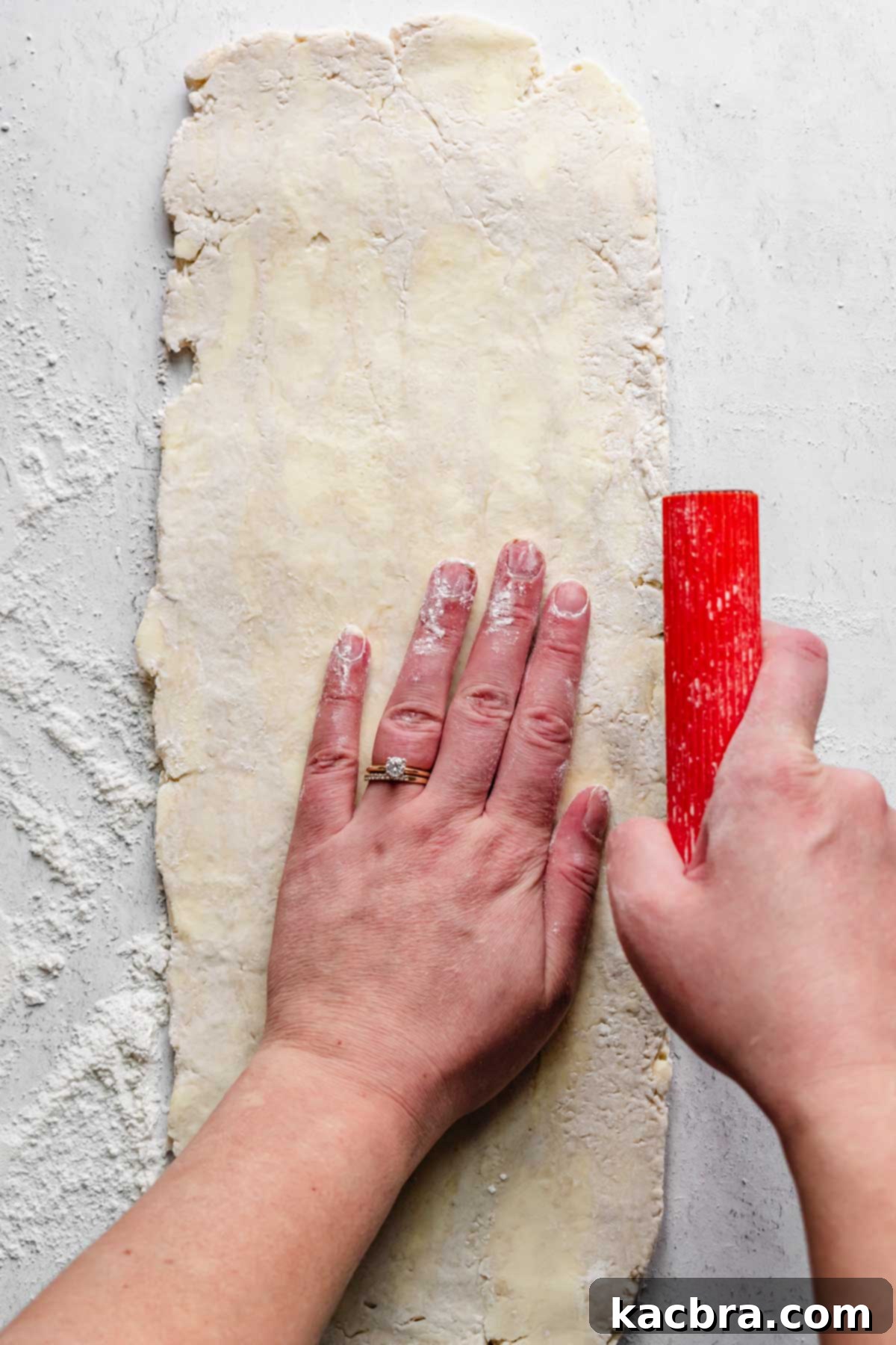 A bench scraper and hand shapes the sides of the rolled out dough.
