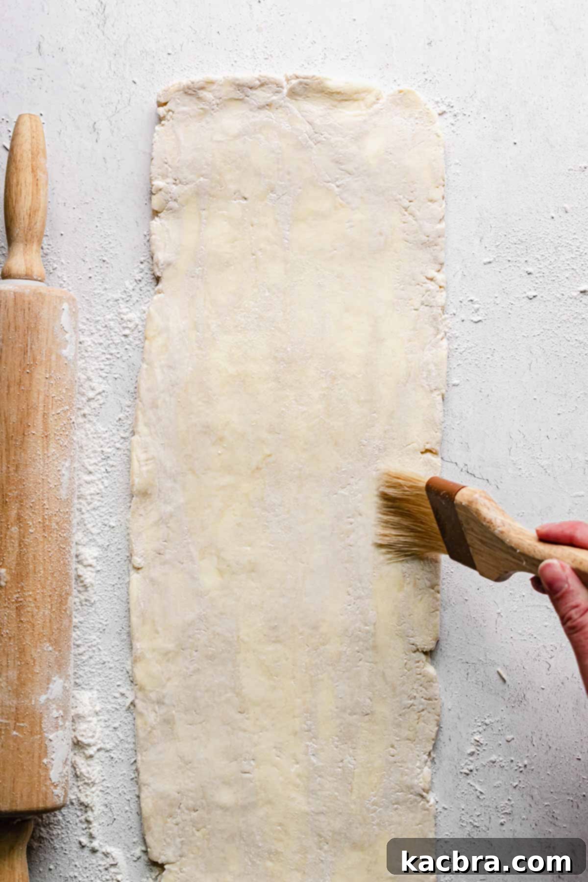 A pastry brush removes flour from the rolled out rough puff pastry.