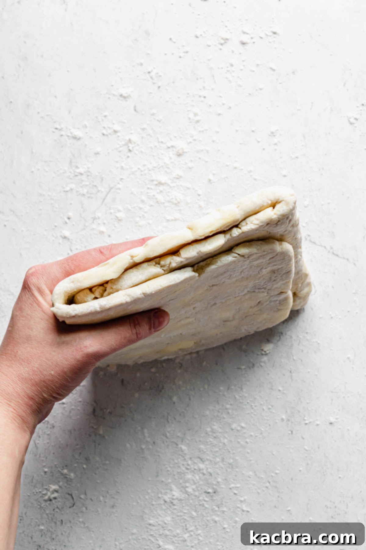 A hand holding the folded dough to show the exposed layers, indicating the proper orientation for the next roll.