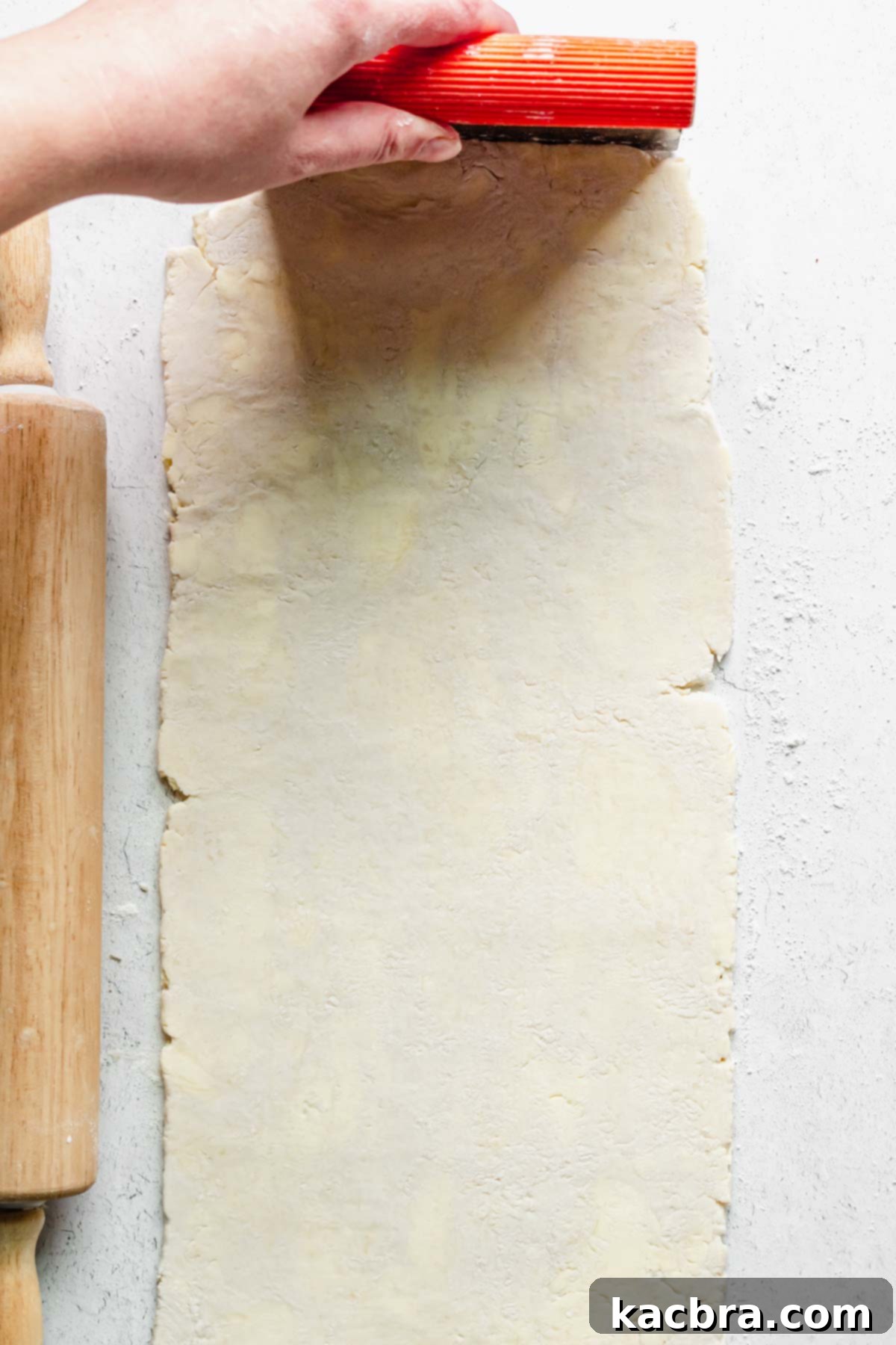 Rough puff pastry dough rolled out in a long rectangle. A bench scraper forms the top of the dough.
