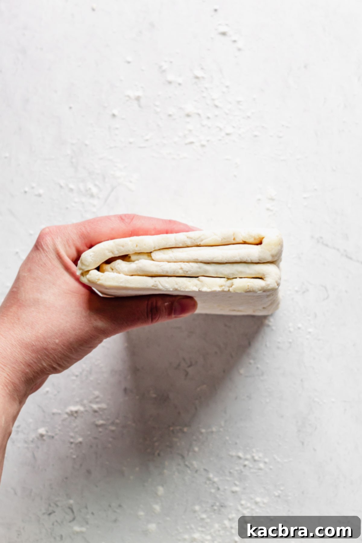 A hand holding the dough to show the exposed layers, indicating the proper orientation for the final roll.