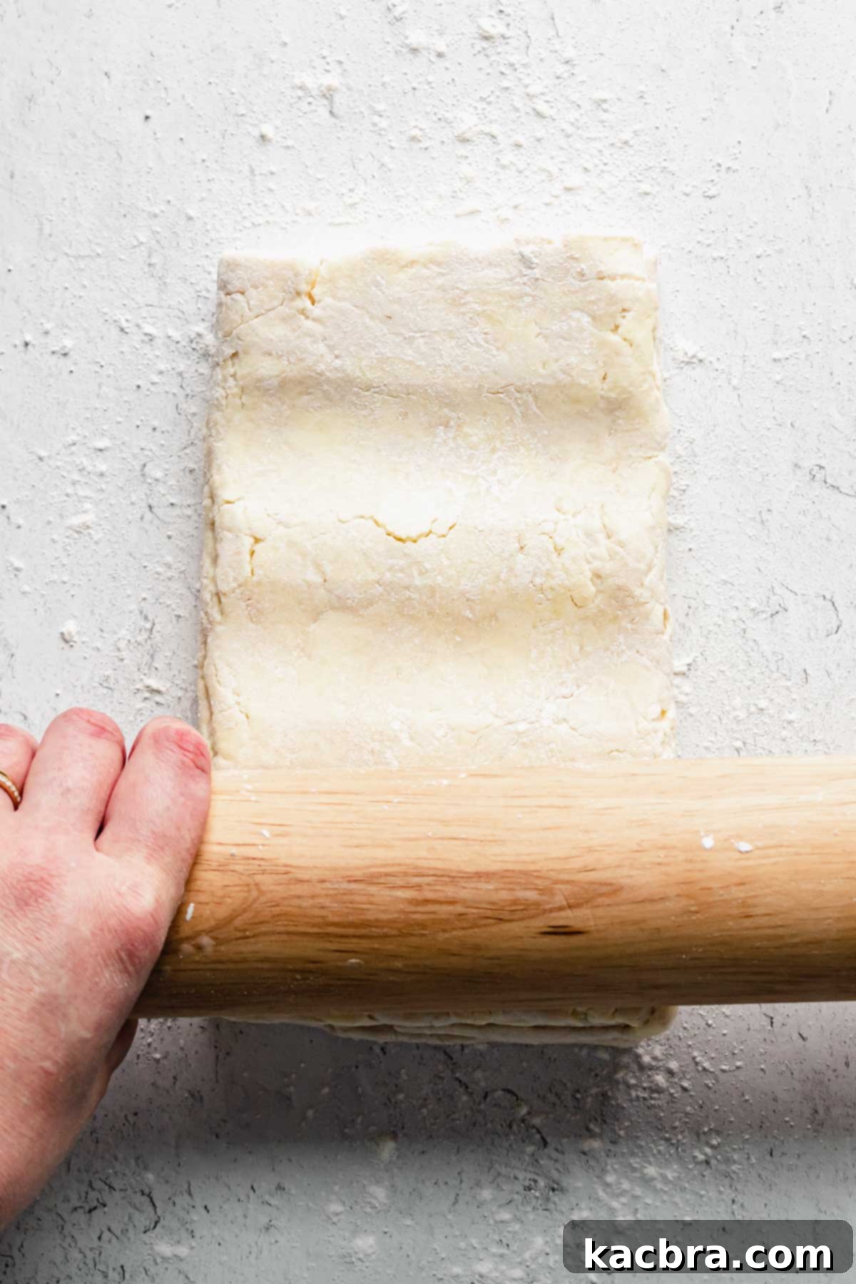 A rolling pin pressing into the dough a few times to gently flatten it before beginning the full rolling process.