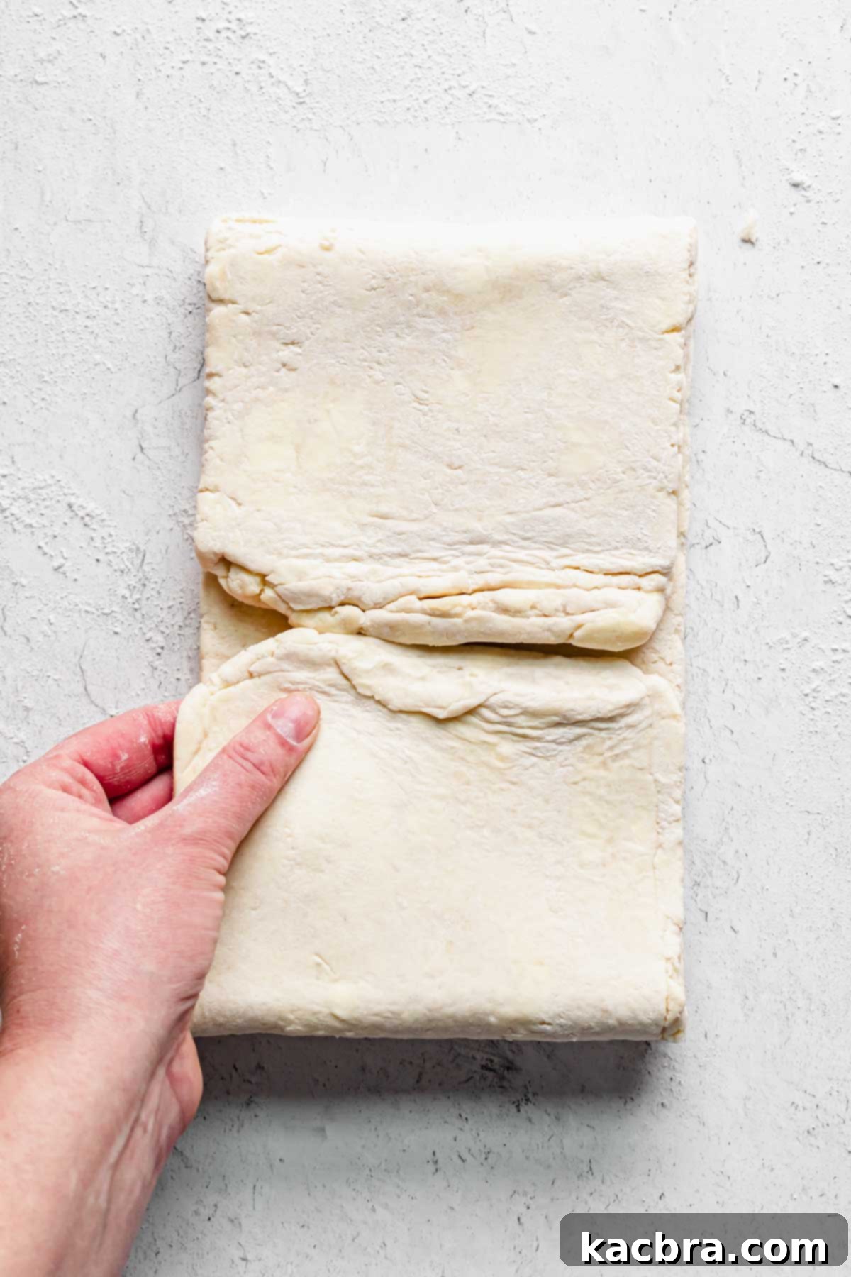 A hand folding the dough into another book fold for the second time, preparing for the final chill.