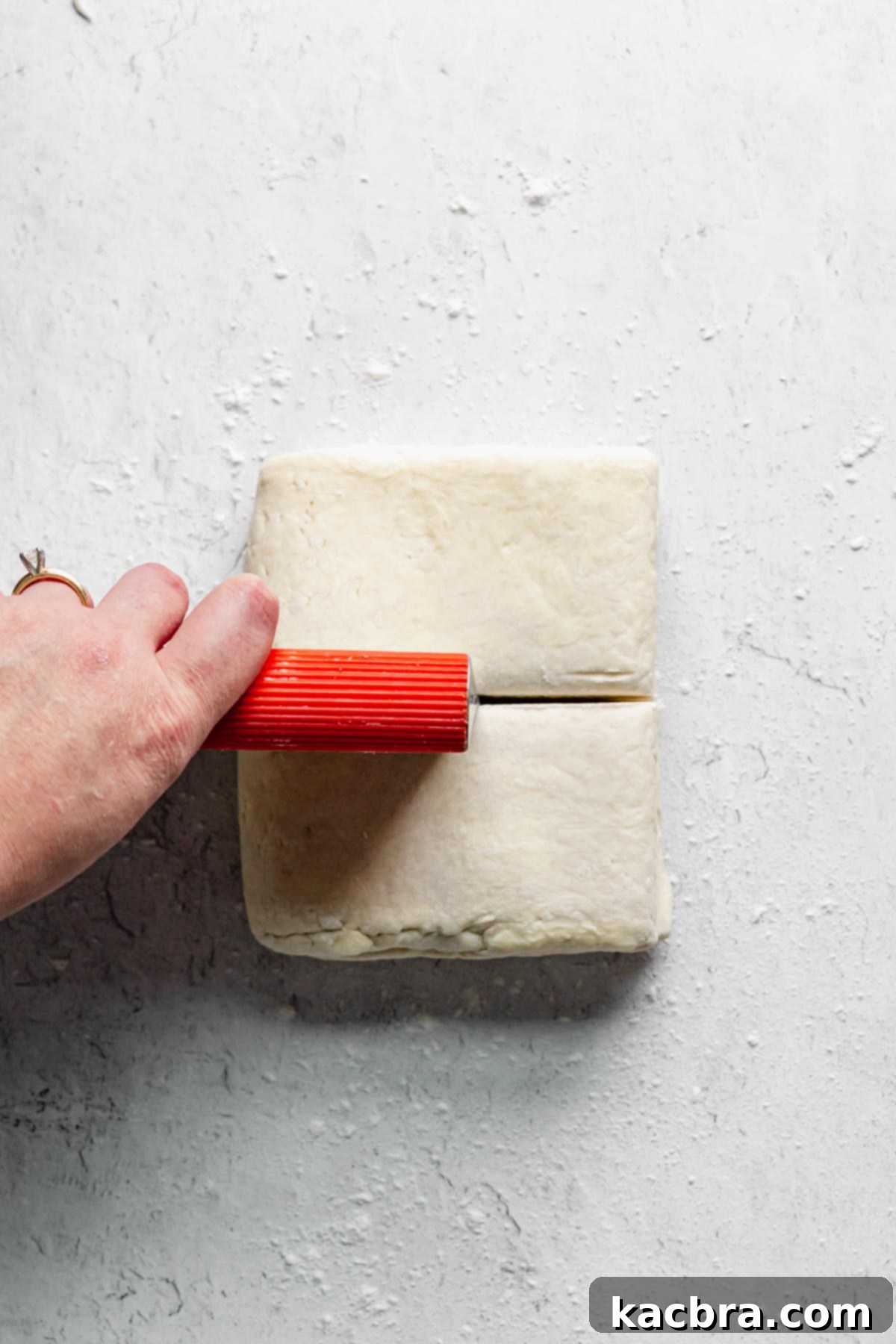 A bench scraper cutting the folded dough in half to create two manageable sheets of rough puff pastry.