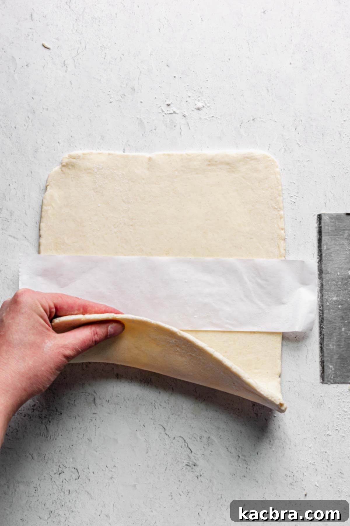 A strip of parchment paper being placed in the center of the rolled-out dough, preparing for folding.