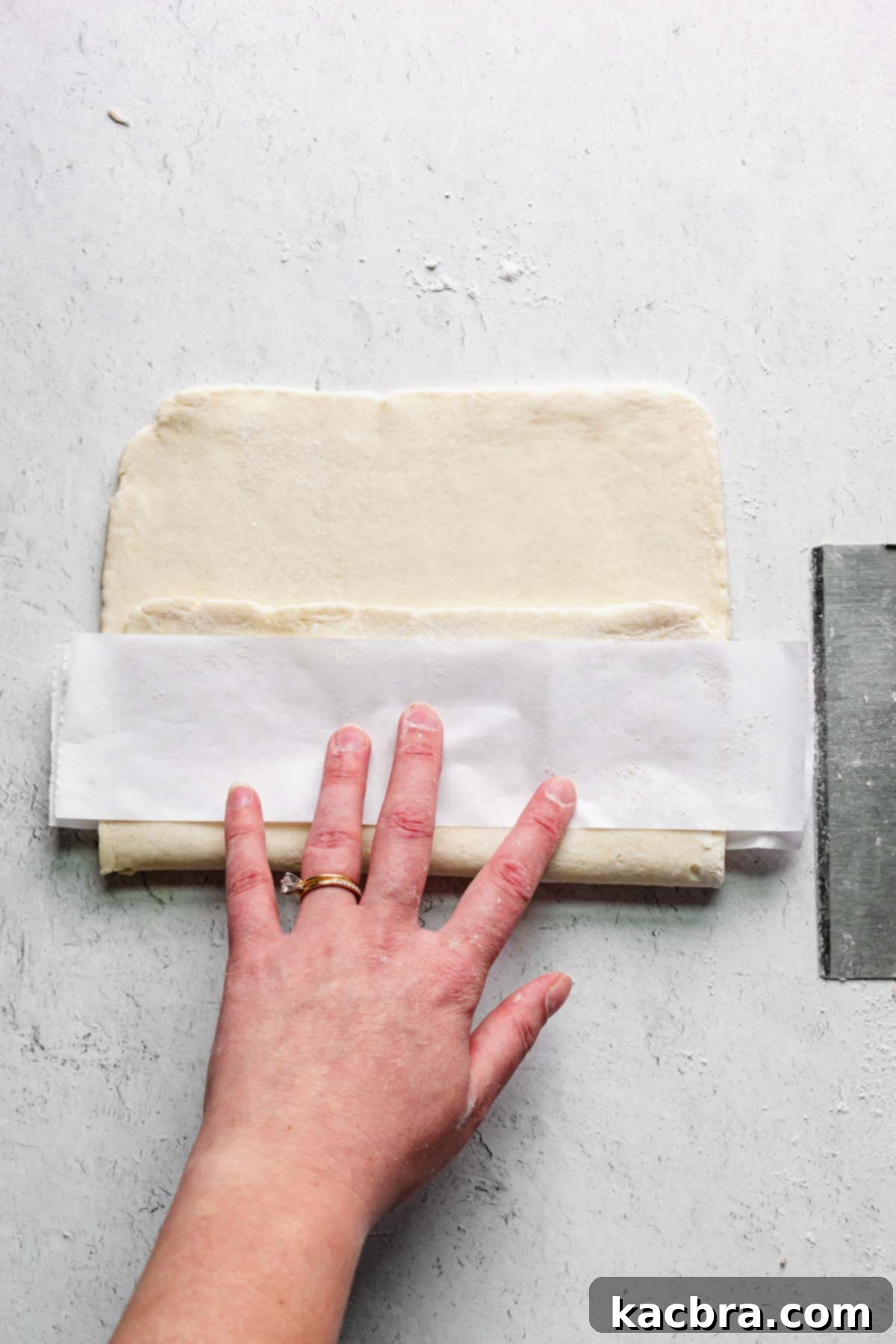 One third of pastry is folded over the parchment, then another strip of parchment is added on top.