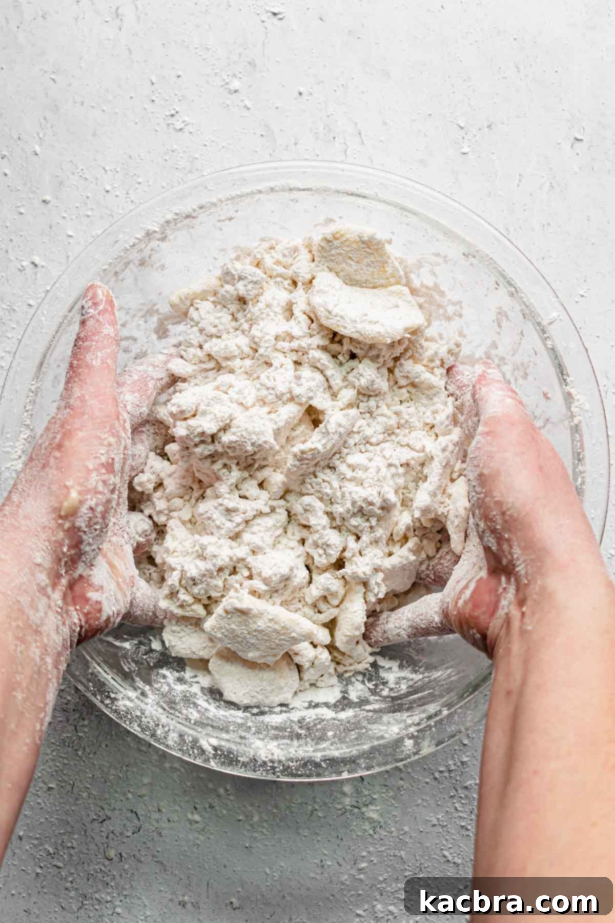 Two hands with 'claw fingers' tossing the butter, flour, and water mixture to combine.