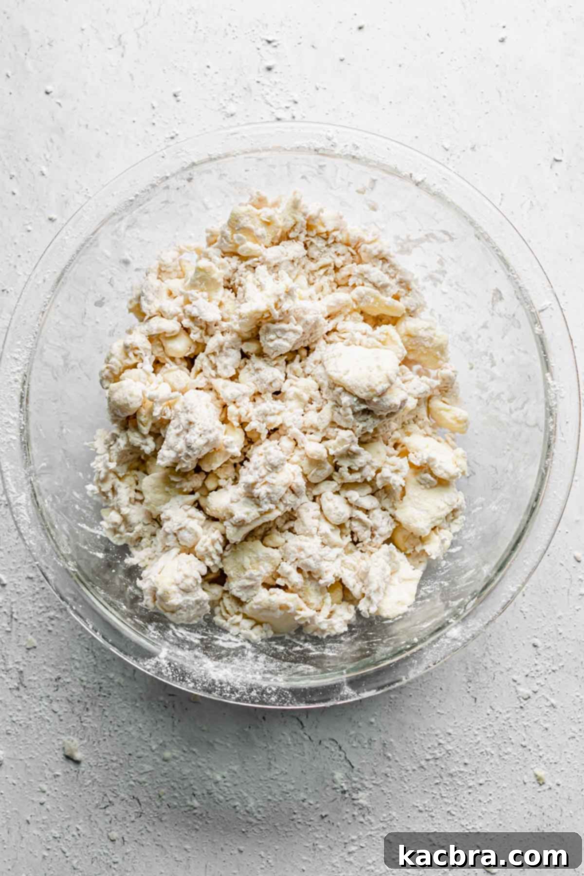 Shaggy dough in a bowl after about five tablespoons of water have been added, showing a crumbly texture.