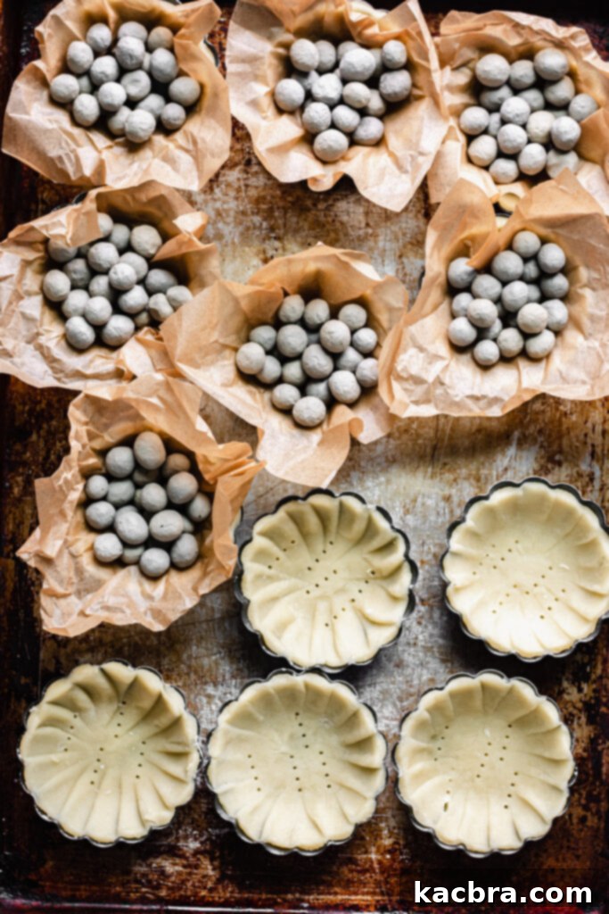 Overhead shot of tartlet shells being filled with parchment and pie weights