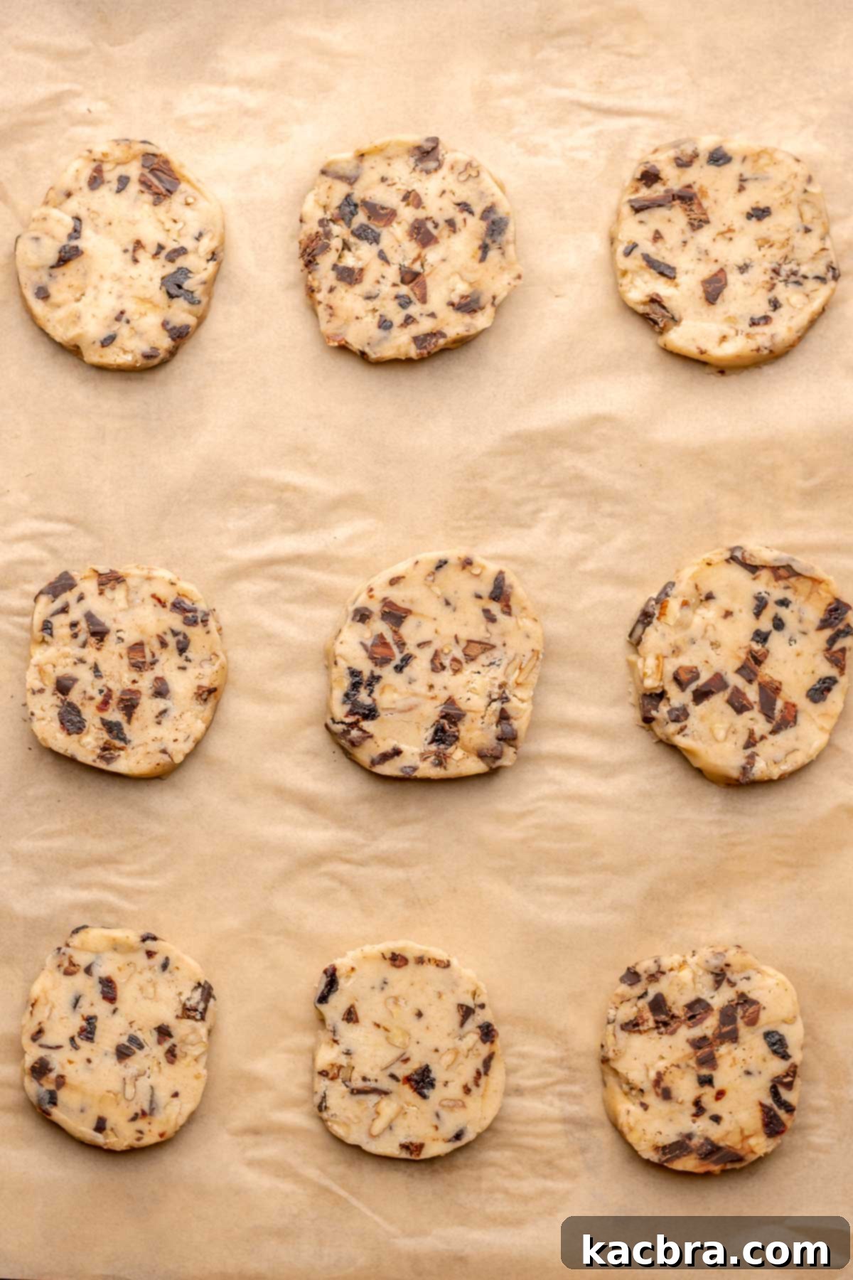 Unbaked cookie dough slices arranged on a parchment-lined baking sheet.