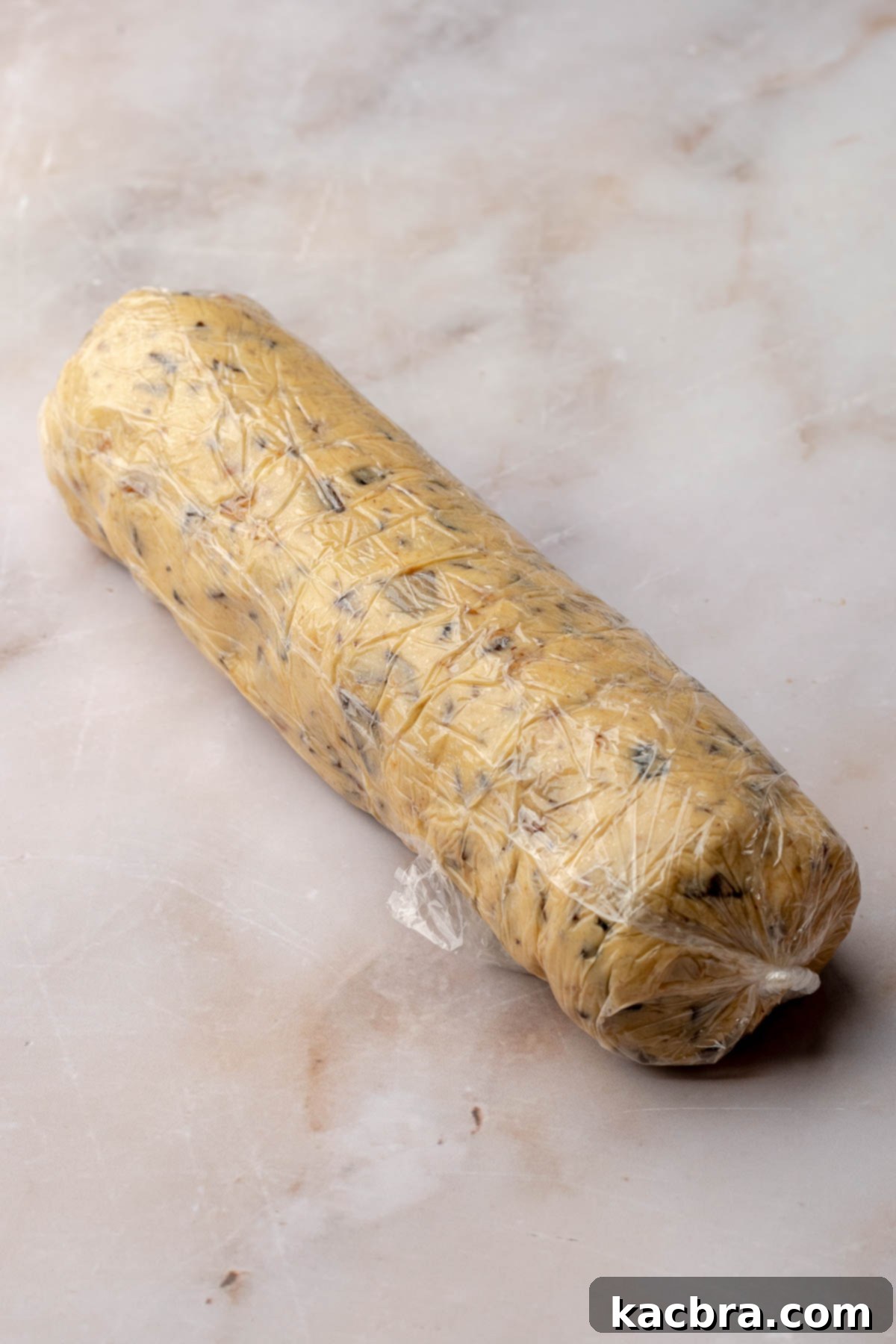 Dough log tightly wrapped in plastic wrap, showing a smooth cylinder.