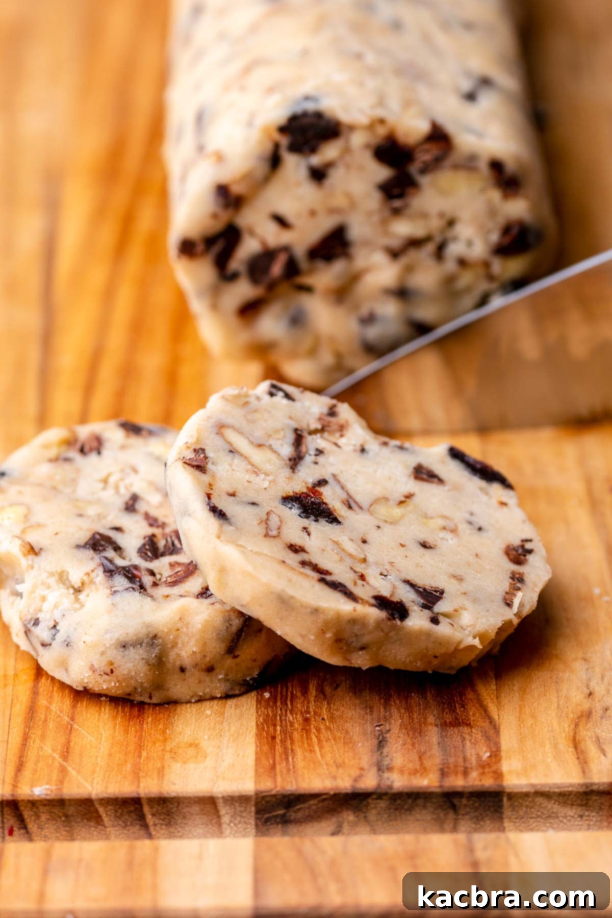 Chef's hand slicing chilled cookie dough log into medallions.