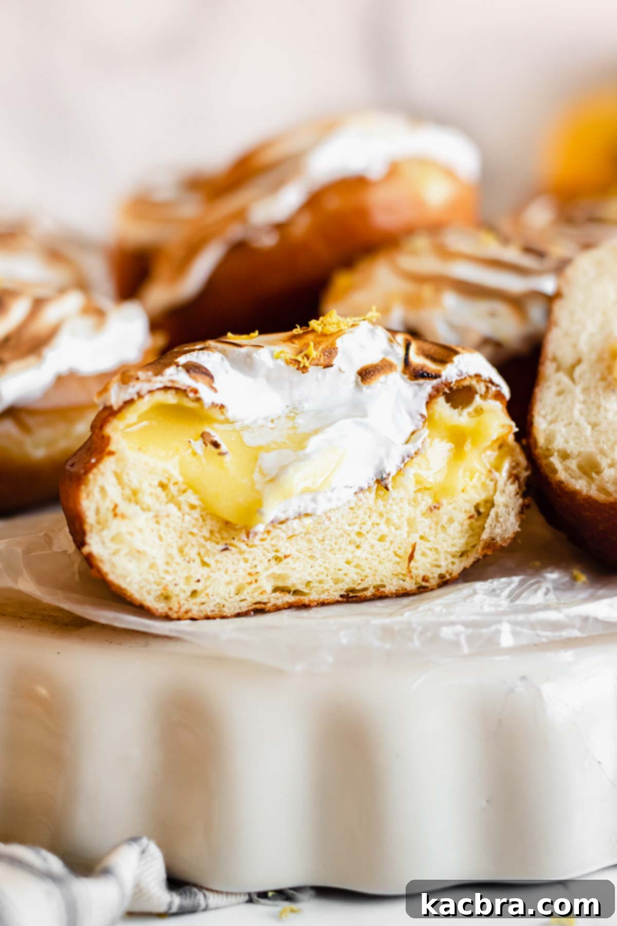 Zesty Meringue Cloud Donuts 2 Straight on shot of the cross section of a lemon filled donut to show the curd inside. A perfectly fried, sugar-dusted brioche donut reveals a generous, bright yellow lemon curd filling, inviting a bite of tangy sweetness.