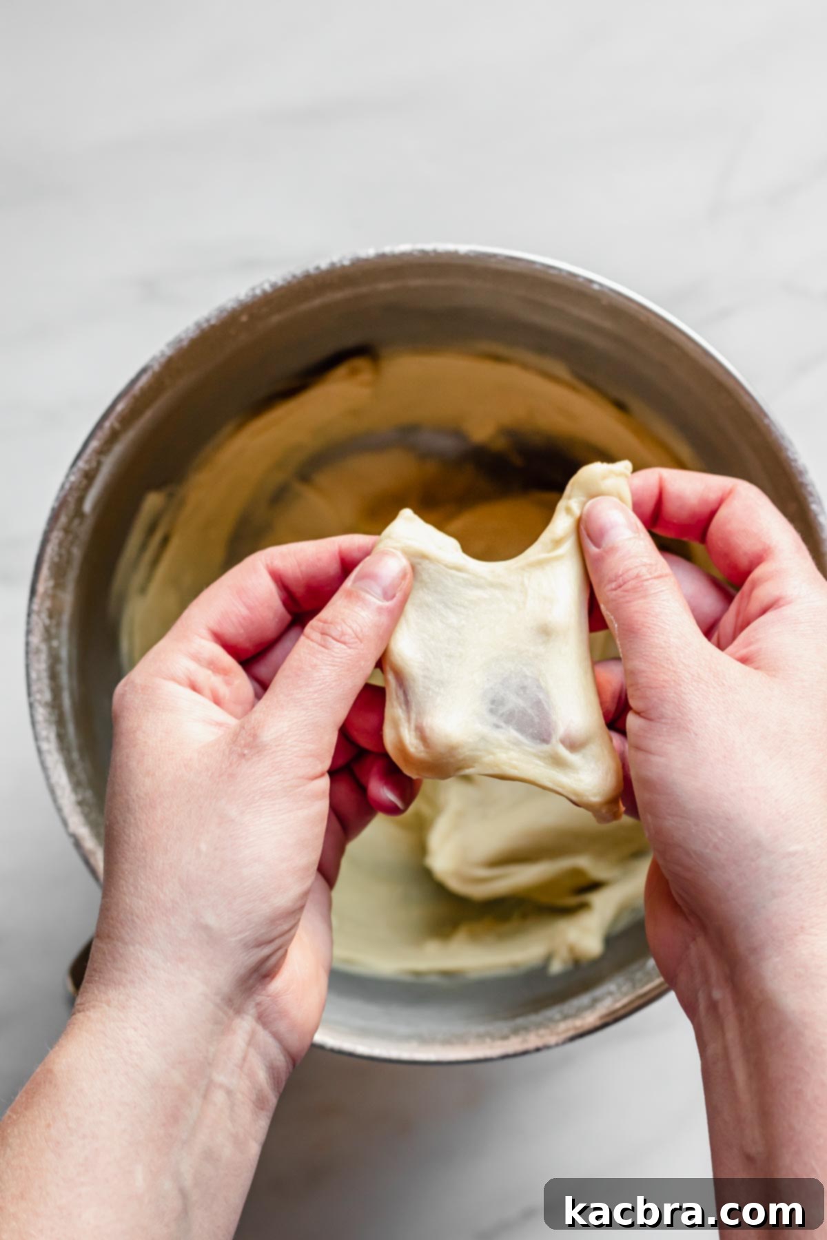 Zesty Meringue Cloud Donuts 5 Hands pull a small piece of dough in four directions for the window pane test.