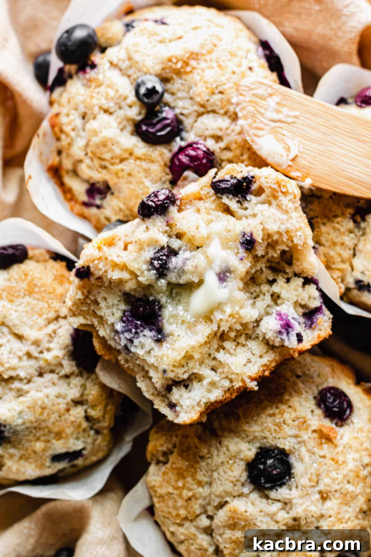 Close up of a fluffy jumbo blueberry muffin split in half with melted butter spread on it, showing the moist interior and abundance of blueberries.