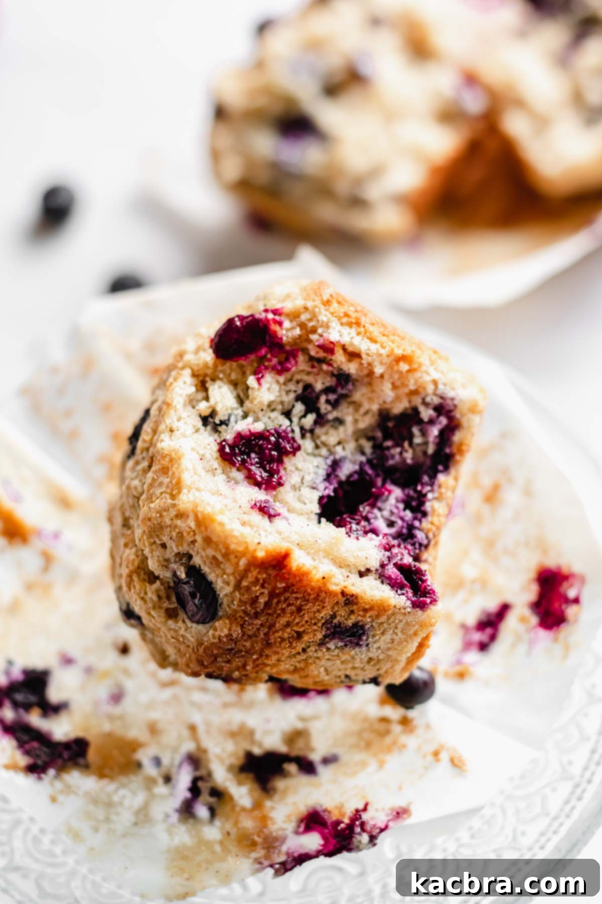 A close-up of a jumbo blueberry muffin with a bite taken out, revealing its moist, tender interior and abundant blueberries.